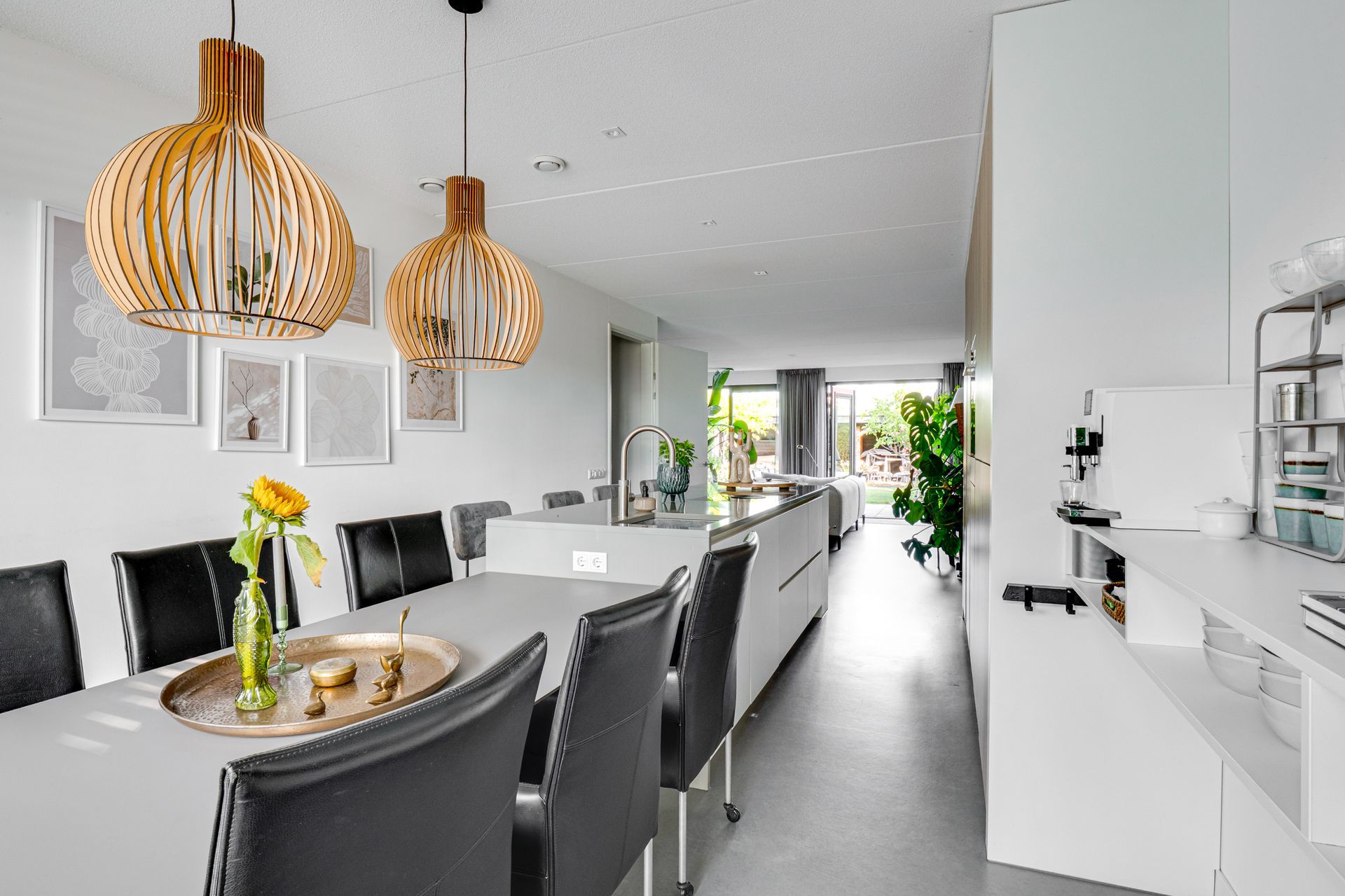 Moderne eetkamer met witte tafel, zwarte stoelen en hanglampen van riet in een lichte, open ruimte.