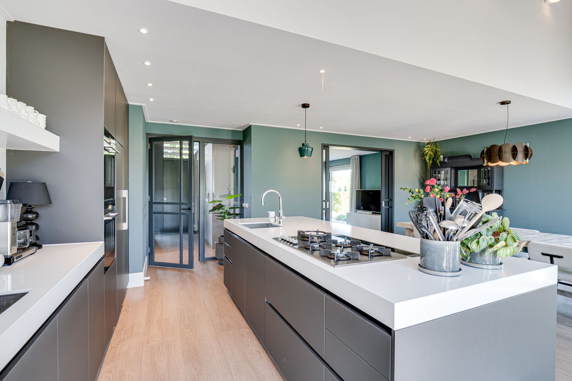 Moderne keuken met groot kookeiland, witte werkbladen, donkere kasten en hanglampen.