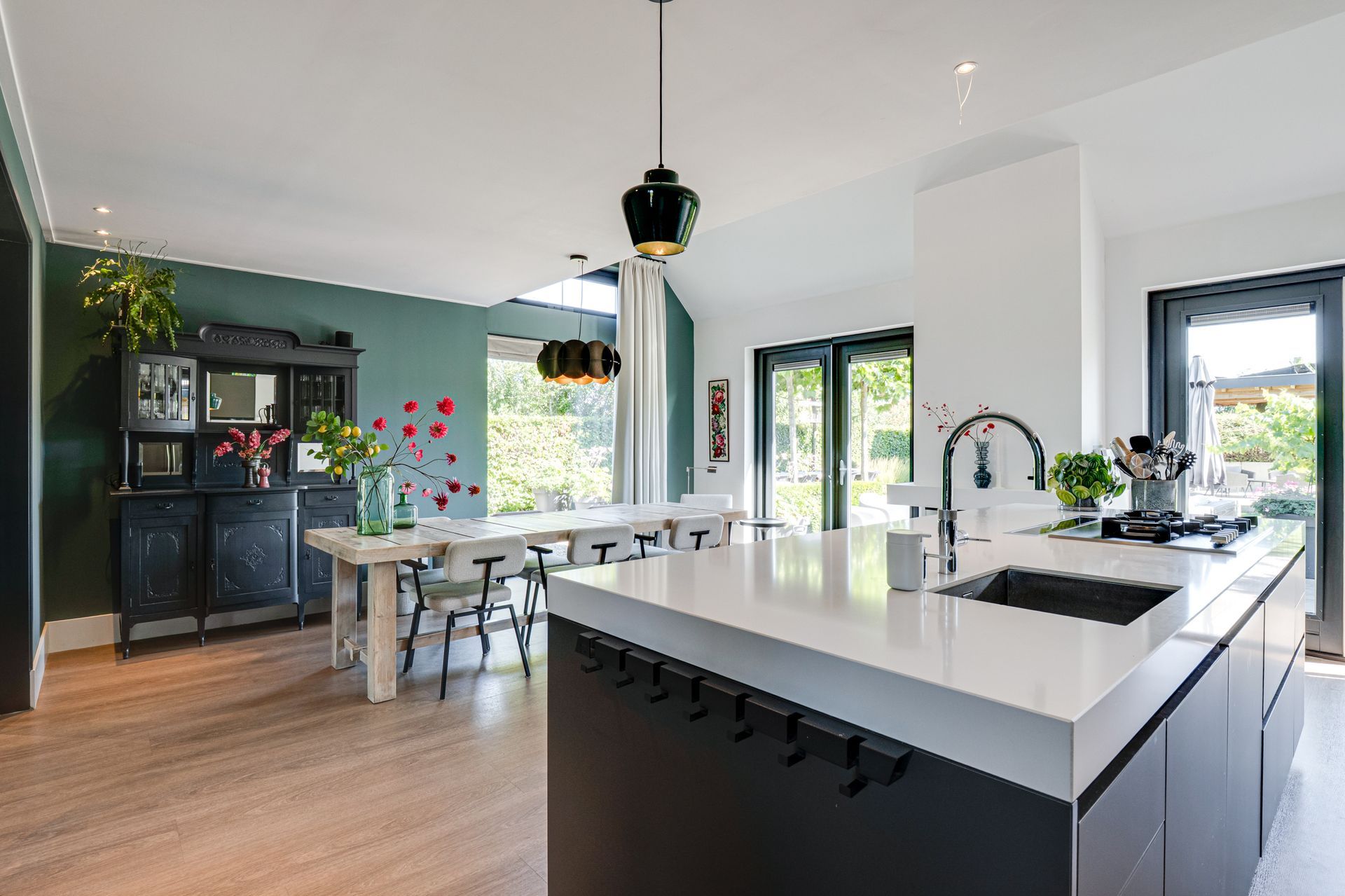 Moderne keuken en eethoek met wit kookeiland, zwarte kasten en grote ramen.