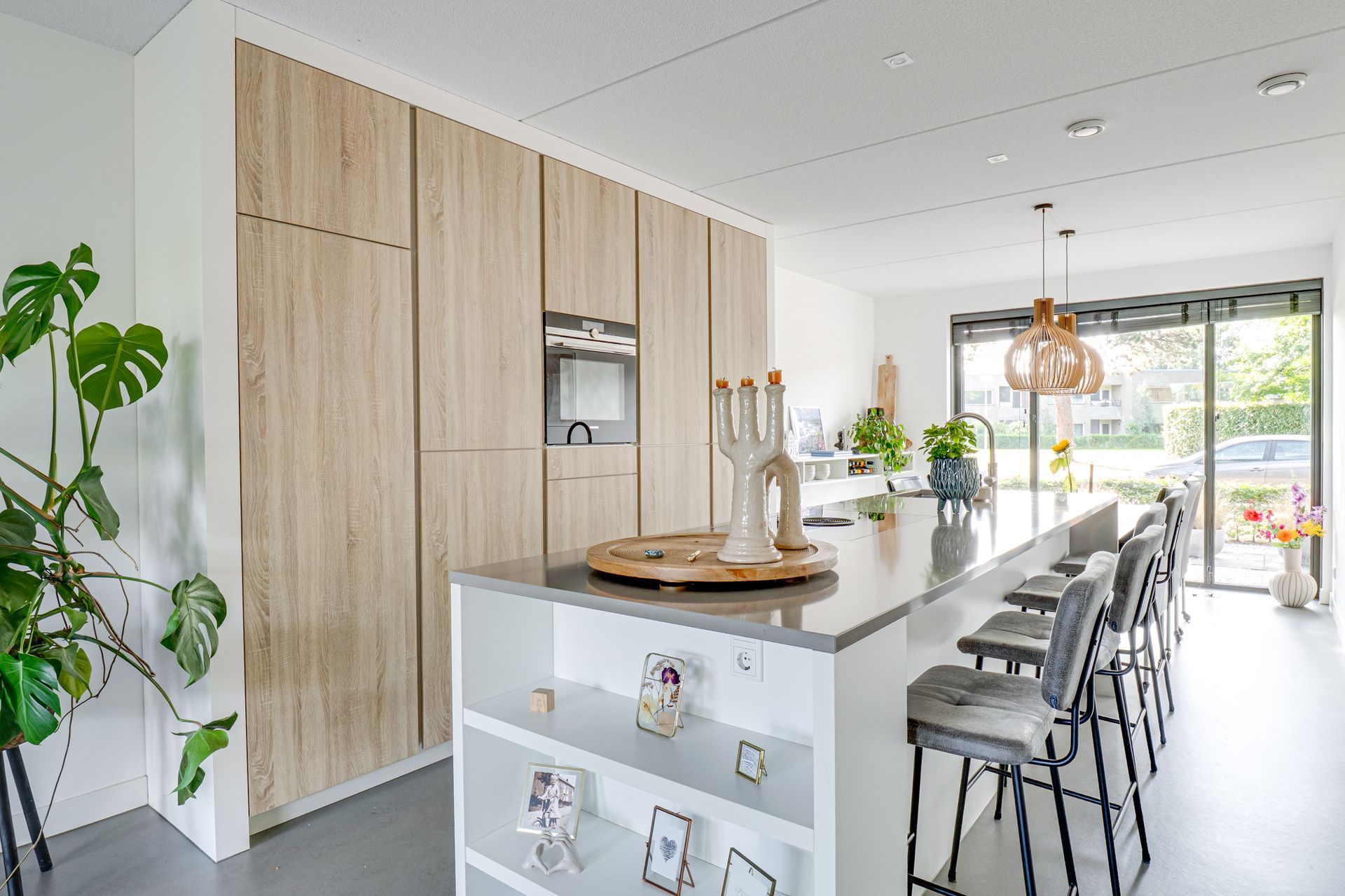 Lichte, moderne keuken met wit kookeiland, houten kasten, barkrukken en kamerplanten.