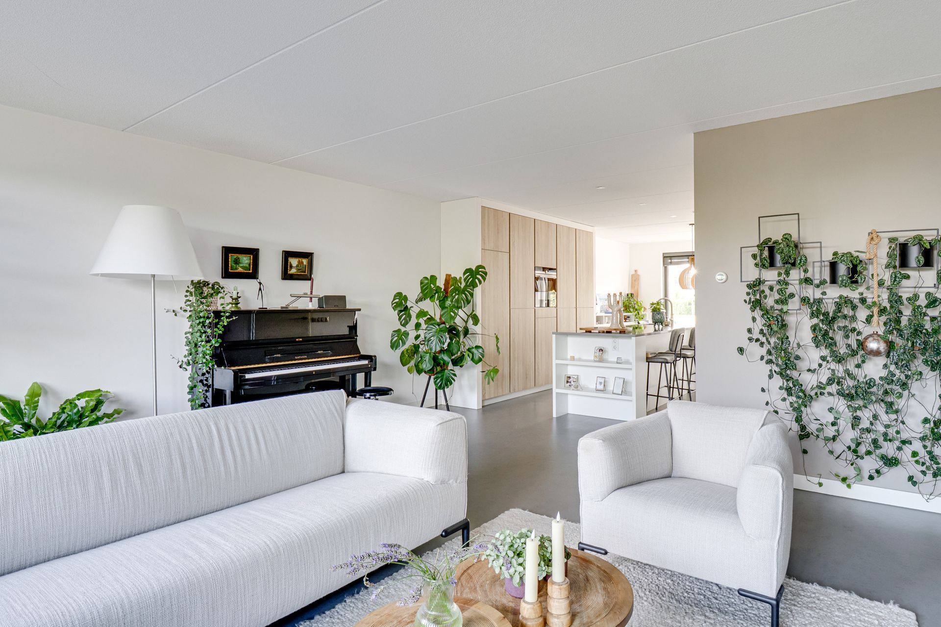 Lichte woonkamer met witte banken, piano, planten en een salontafel in een modern huis.