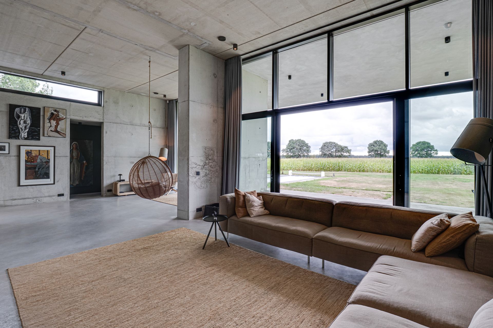 Moderne loft-woonkamer met grote ramen, beige hoekbank en uitzicht op de velden buiten.