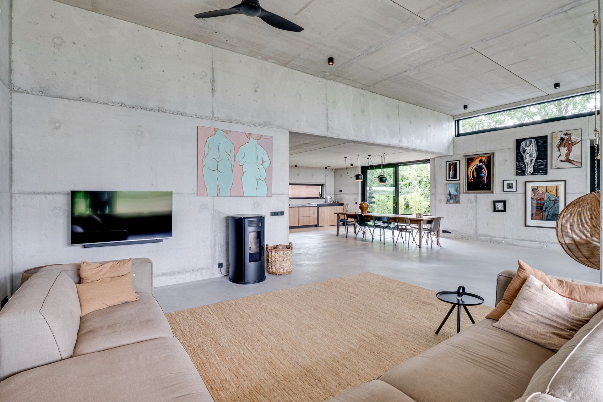 Moderne open woonkamer met beige banken, aan de muur gemonteerde tv en een eethoek op de achtergrond.