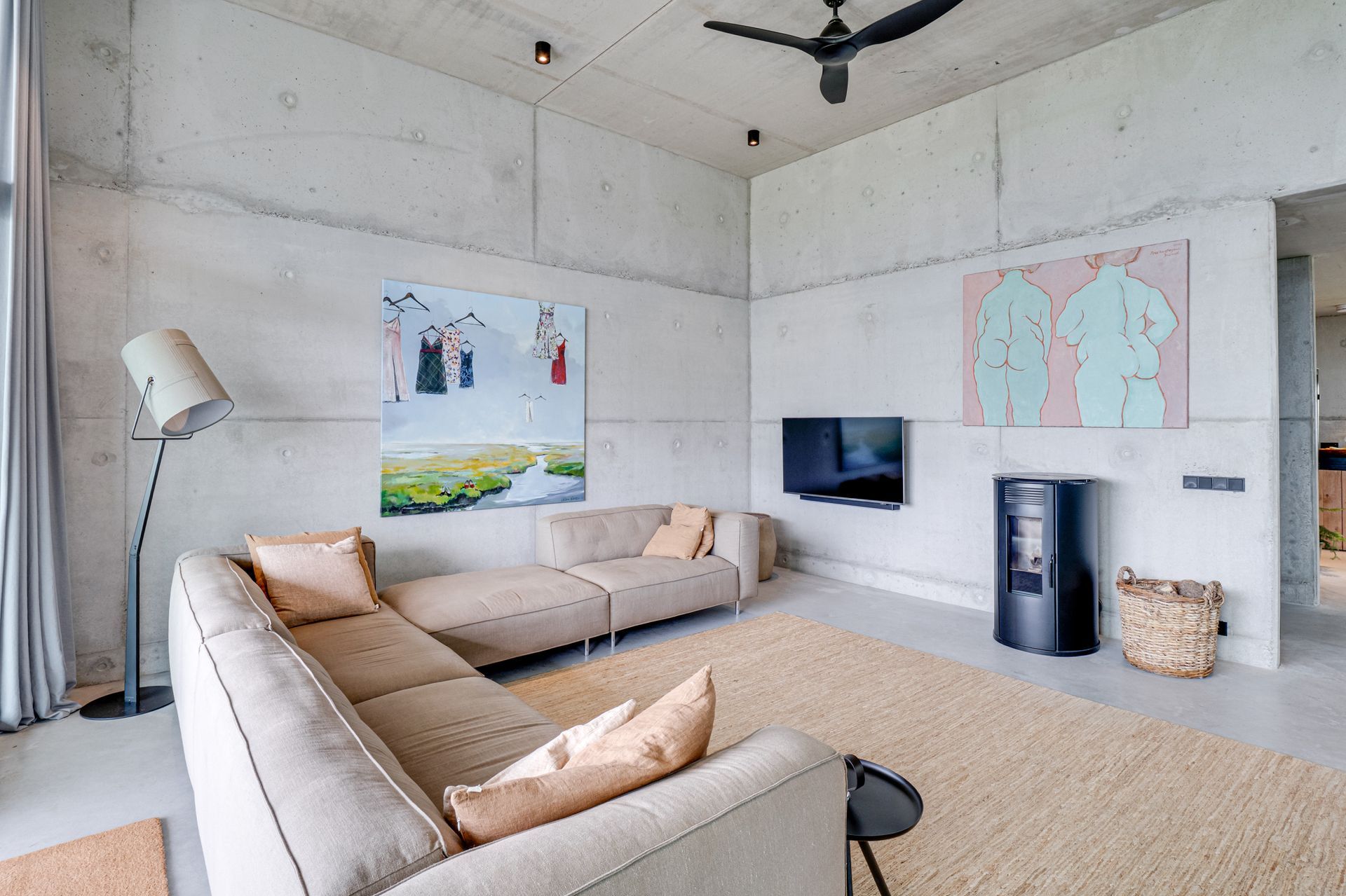 Moderne woonkamer met beige hoekbank, aan de muur gemonteerde tv, betonnen muren en kleurrijke kunstwerken.