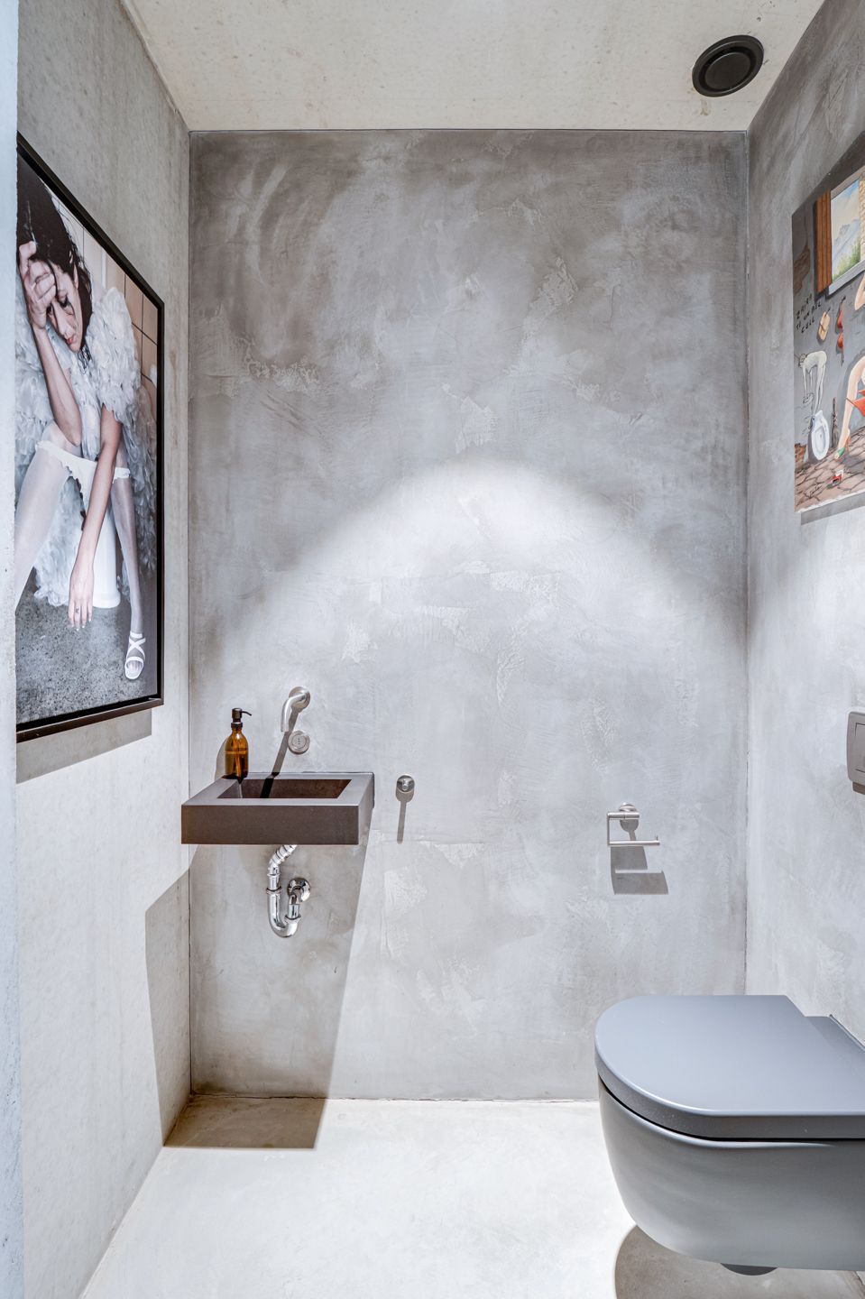 Minimalistische badkamer met grijze muren, een aan de muur gemonteerde wastafel en een gedeeltelijk zichtbaar toilet.