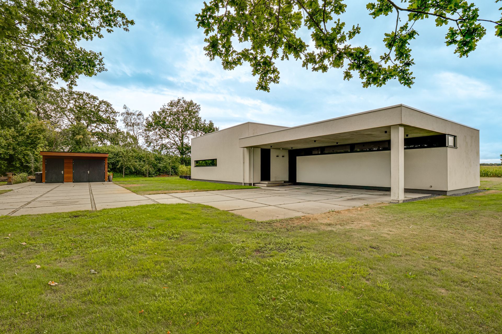 Moderne witte woning met overdekte carport naast een grasveld en bomen.