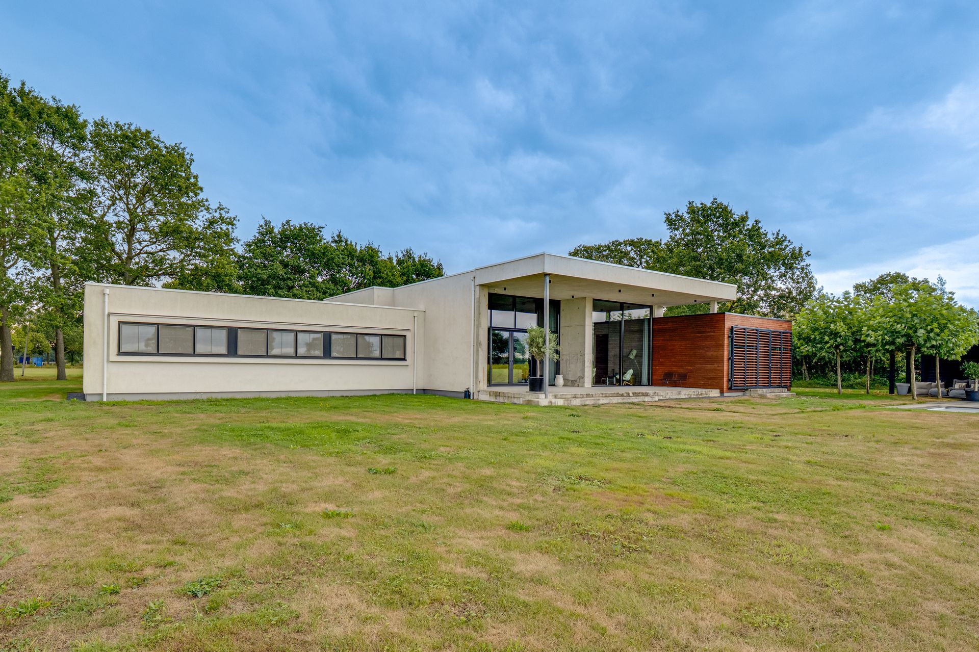 Moderne bungalow met grote ramen, witte gevel en een grasveld onder een blauwe hemel.