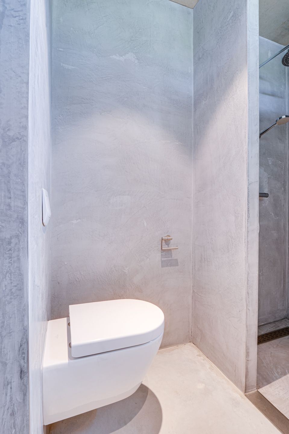 Kleine, moderne badkamer met een wit wandtoilet en grijze tegelwanden.