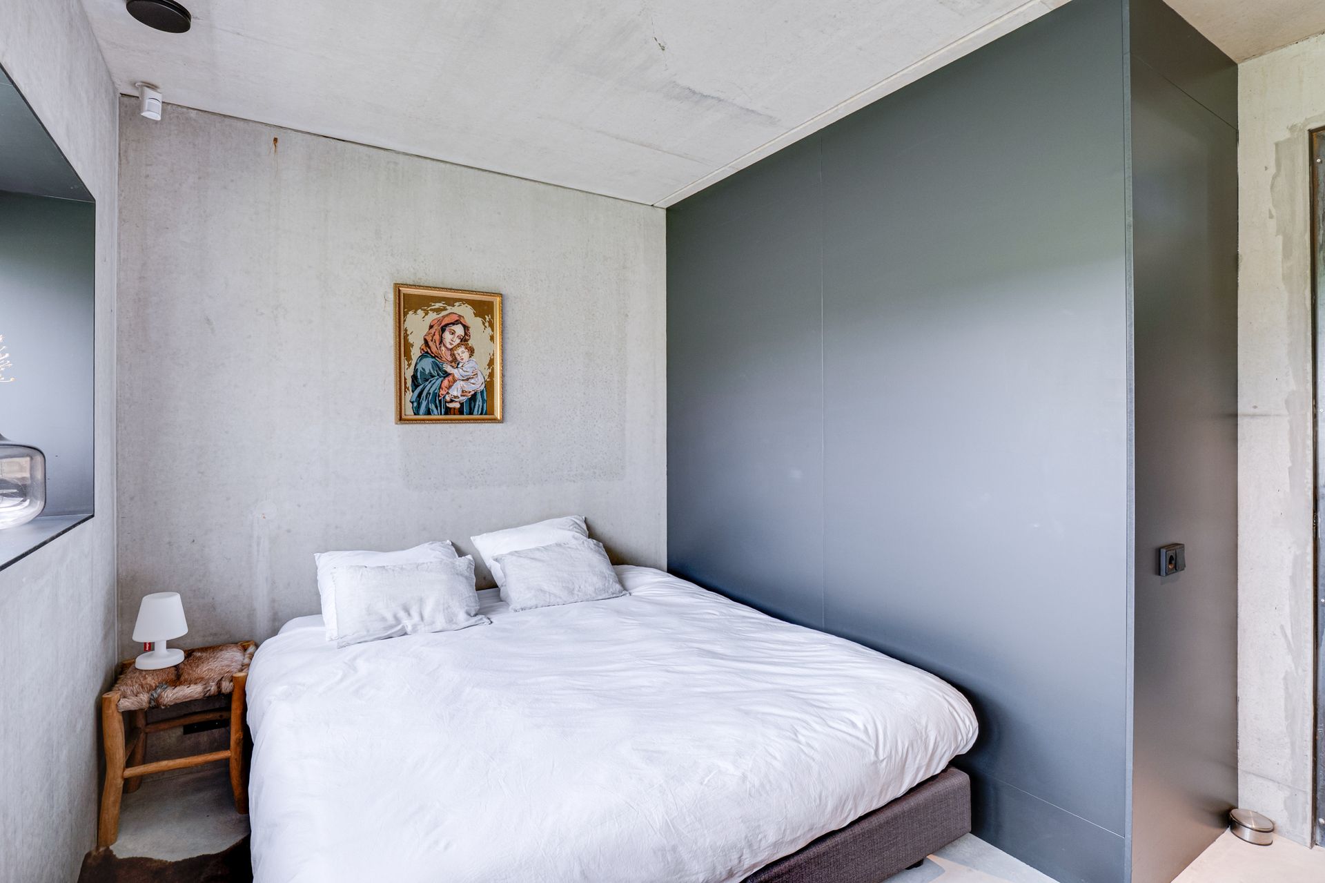 Minimalistische slaapkamer met wit bed, houten nachtkastje en grijze accentmuur.