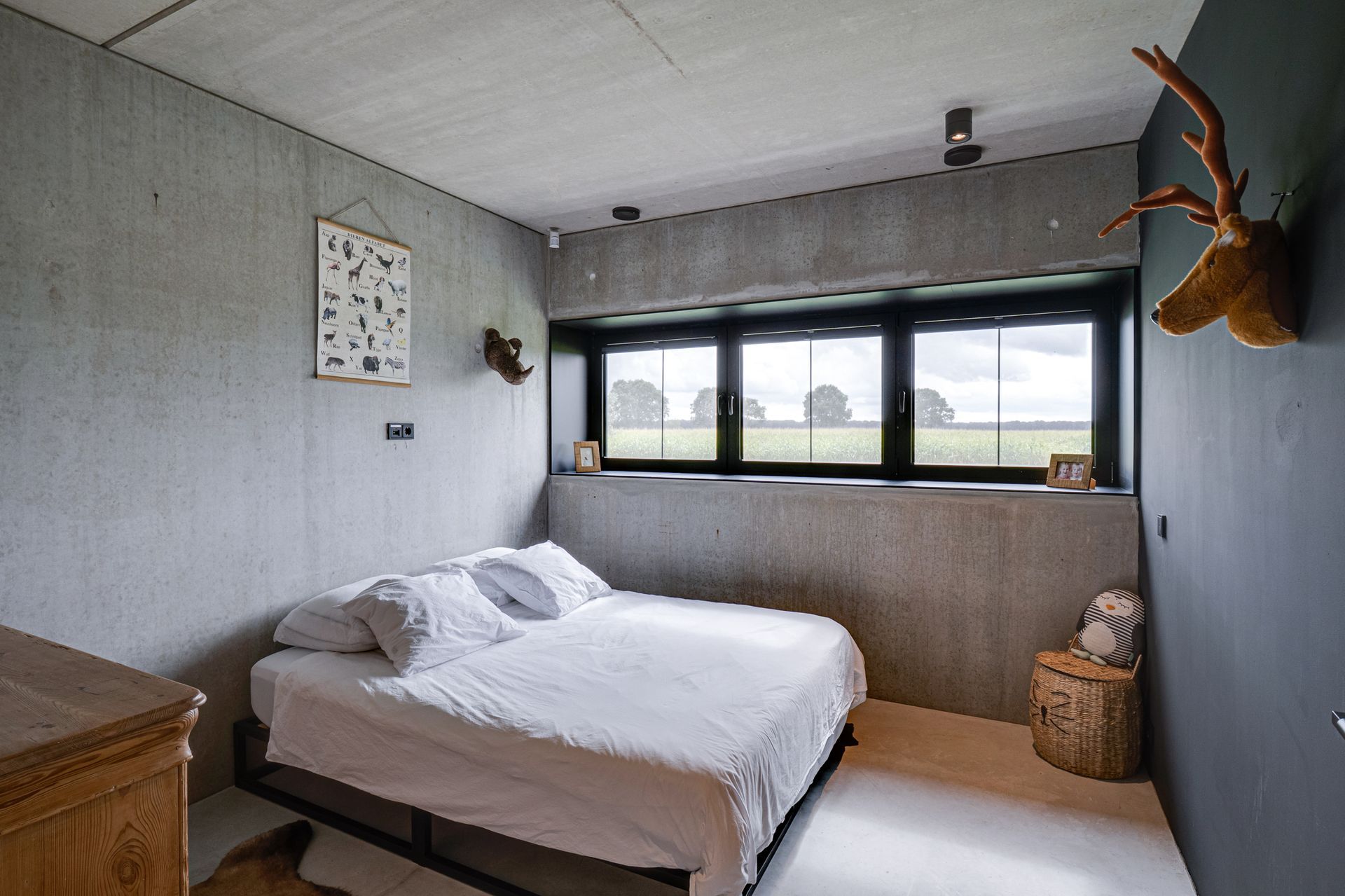 Minimalistische slaapkamer met een bed, grijze muren, een groot raam en een opgehangen hertenkop als decoratie.