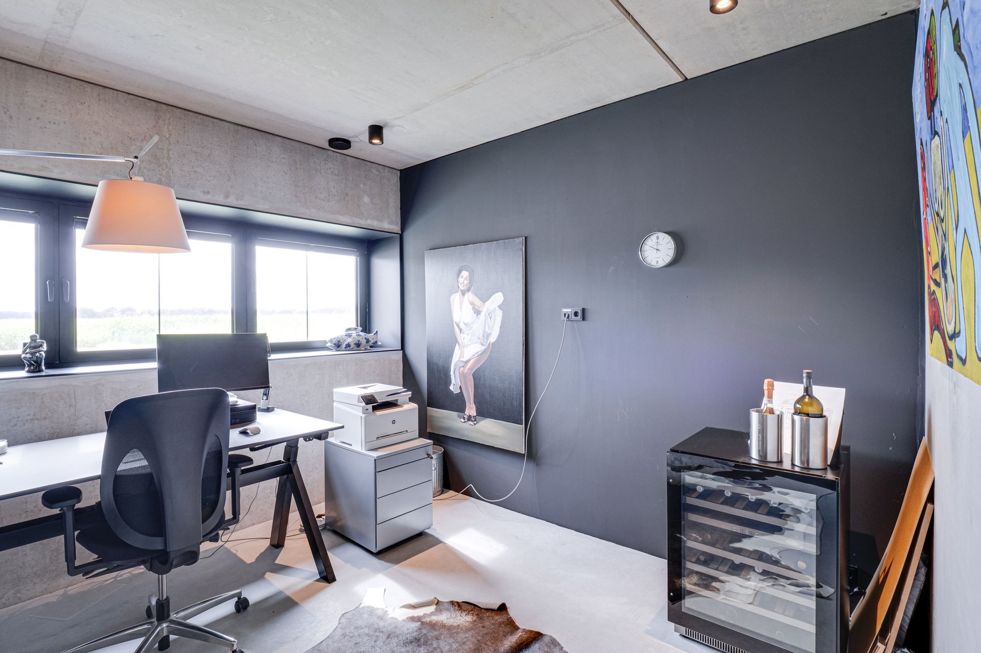 Moderne thuiswerkplek met bureau, stoel, computer, wanddecoratie en een grijze accentmuur.