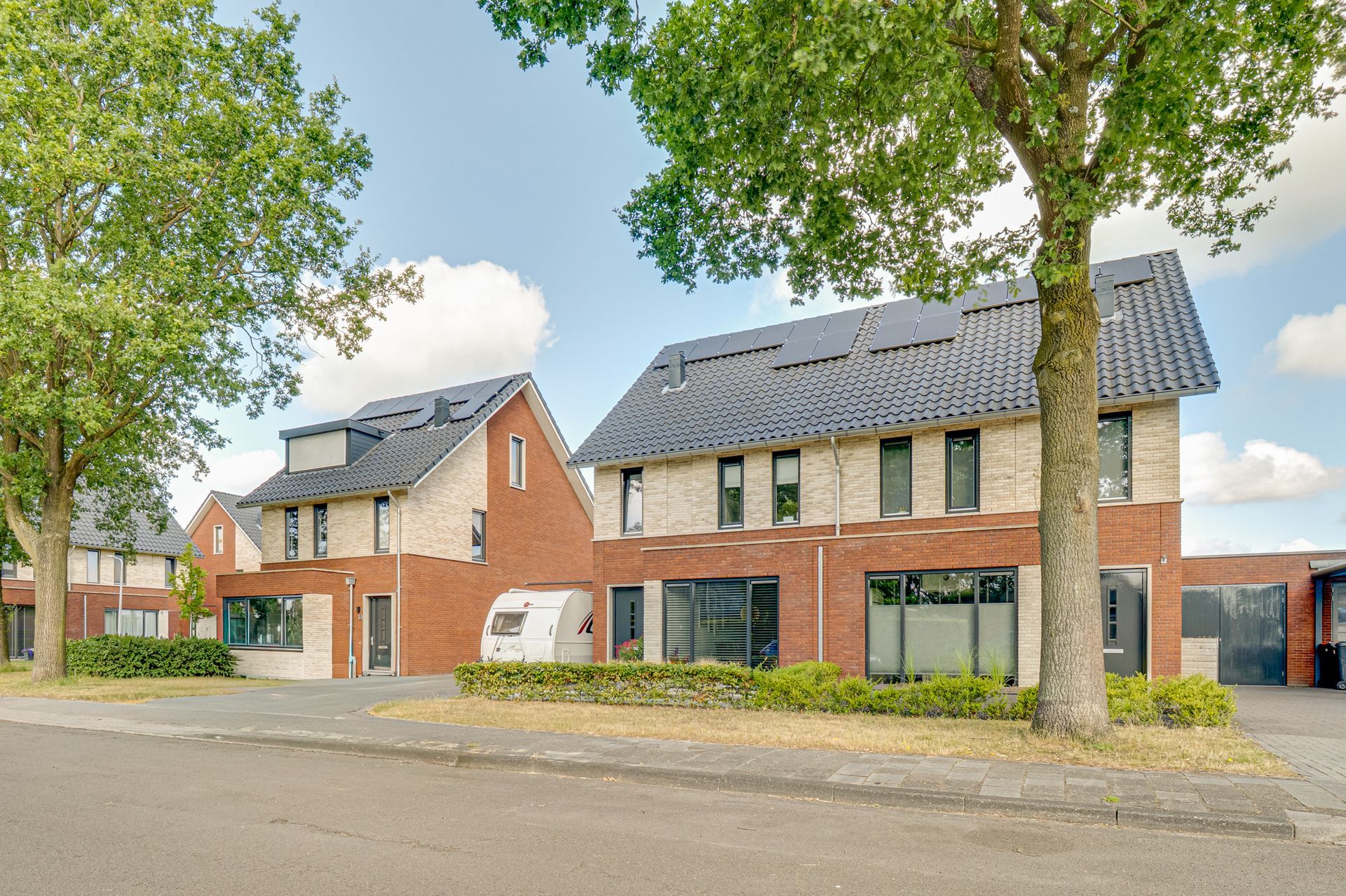 Moderne bakstenen appartementengebouwen met bomen en een straat ervoor.