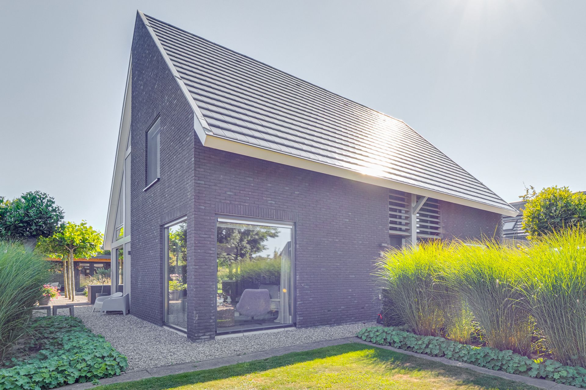 Moderne bakstenen woning met schuin dak, grote ramen en een zonnige tuin.