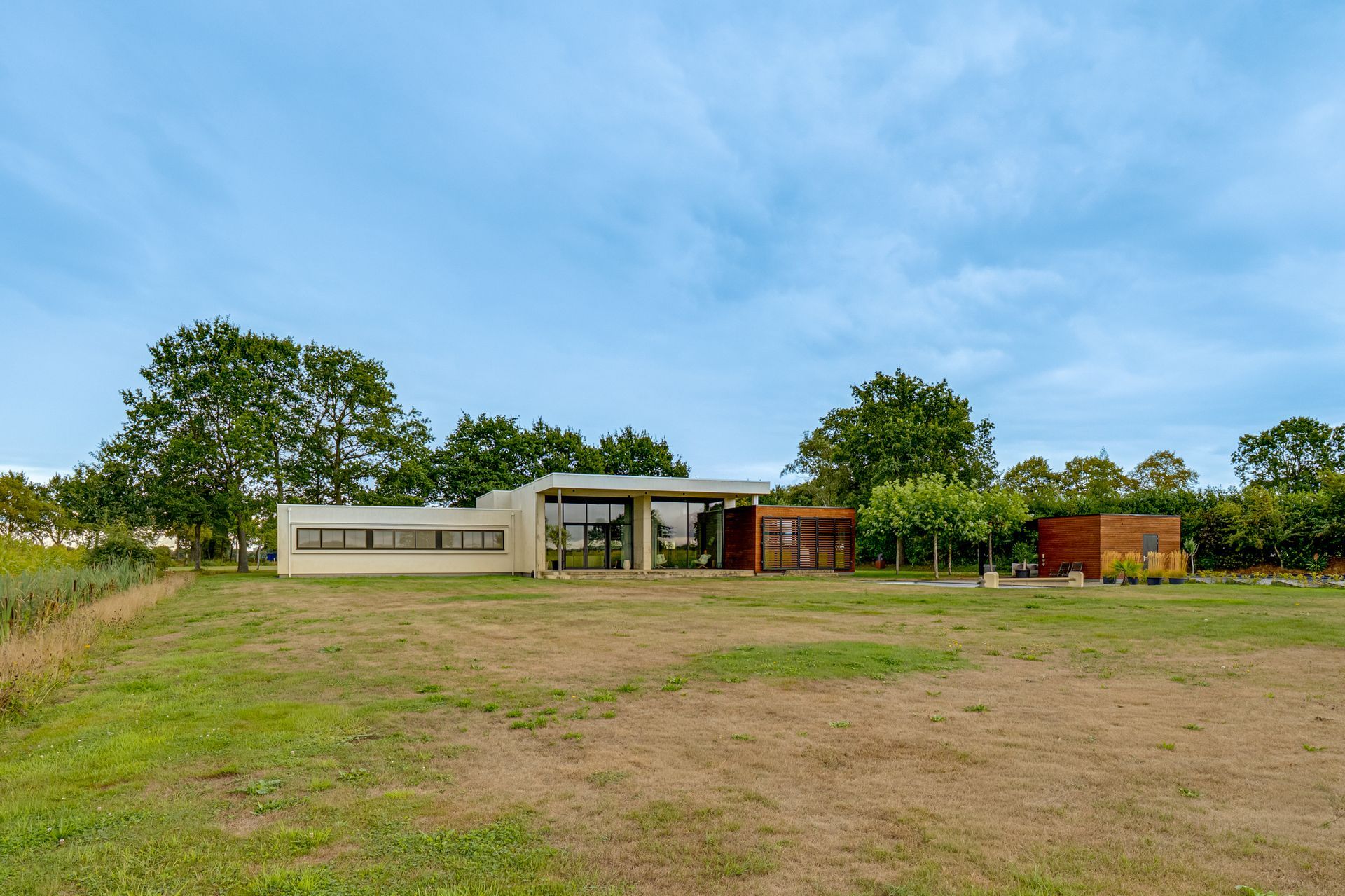 Een uitgestrekt grasveld met een klein modern gebouw en bomen onder een blauwe hemel.