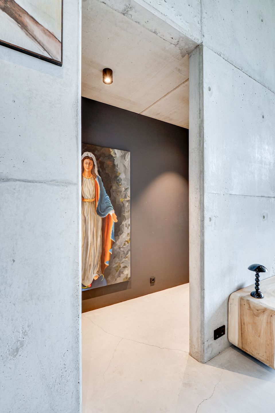 Moderne betonnen hal met een groot portret, een donkere accentmuur en een kleine houten bank met een zwart beeldhouwwerk.