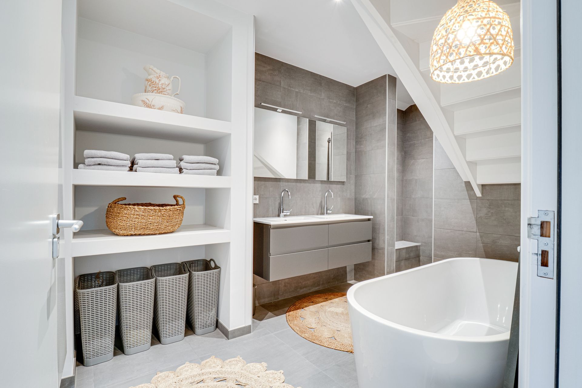 Lichte, moderne badkamer met bad, wastafel, planken en gevlochten manden onder de trap.