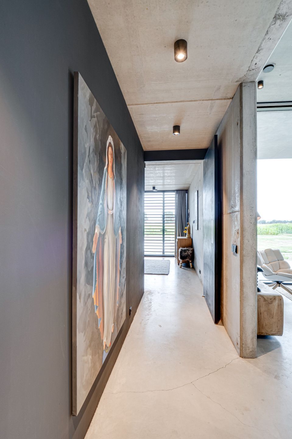 Moderne hal met donkere muren, witte vloer, abstracte muurkunst en een open uitzicht op een lichte buitenruimte.