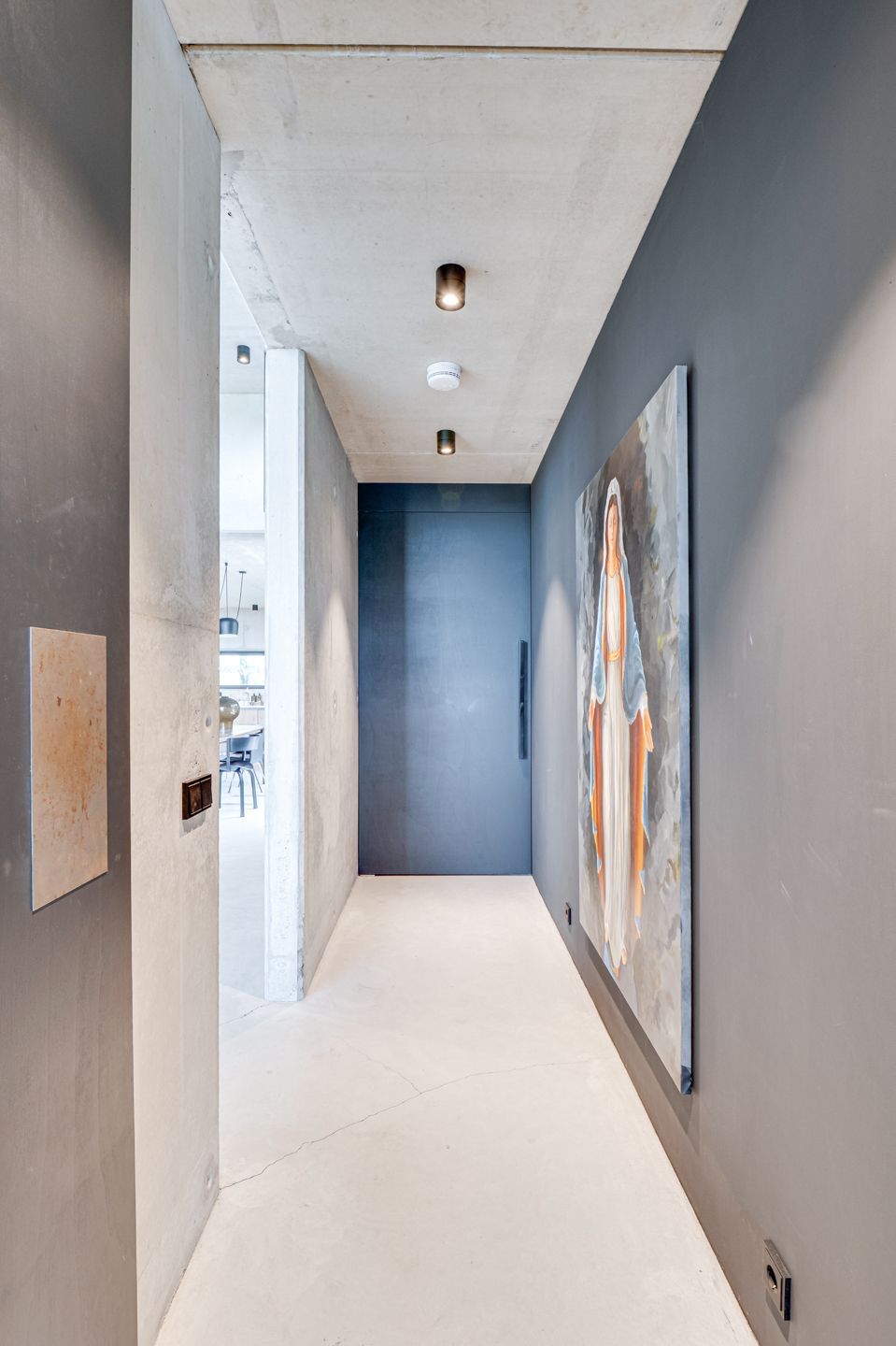 Smalle grijze gang met witte vloer en abstracte muurkunst.