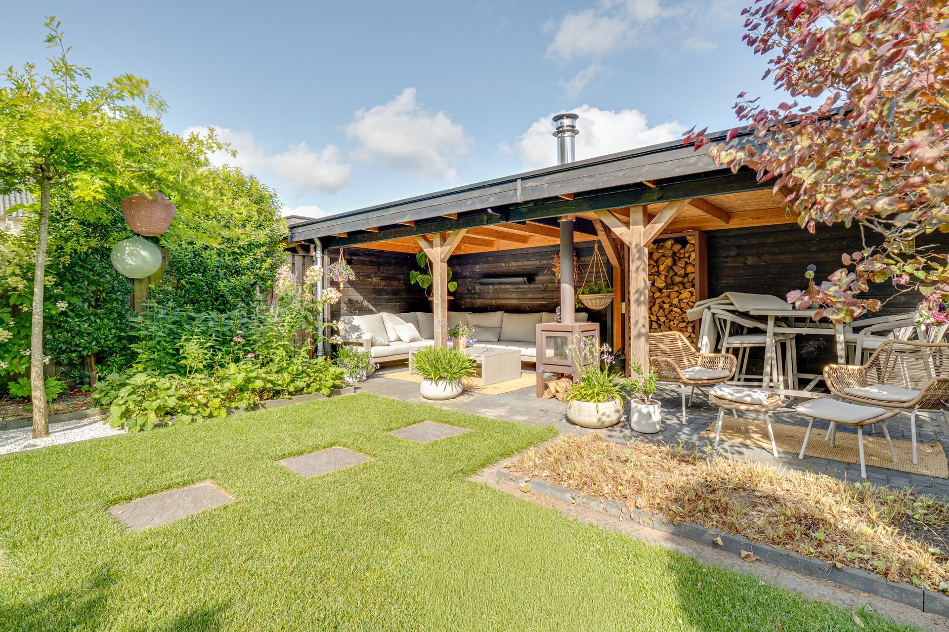 Zonnig terras in de achtertuin met houten pergola, tuinmeubilair en een groen gazon met stapstenen.
