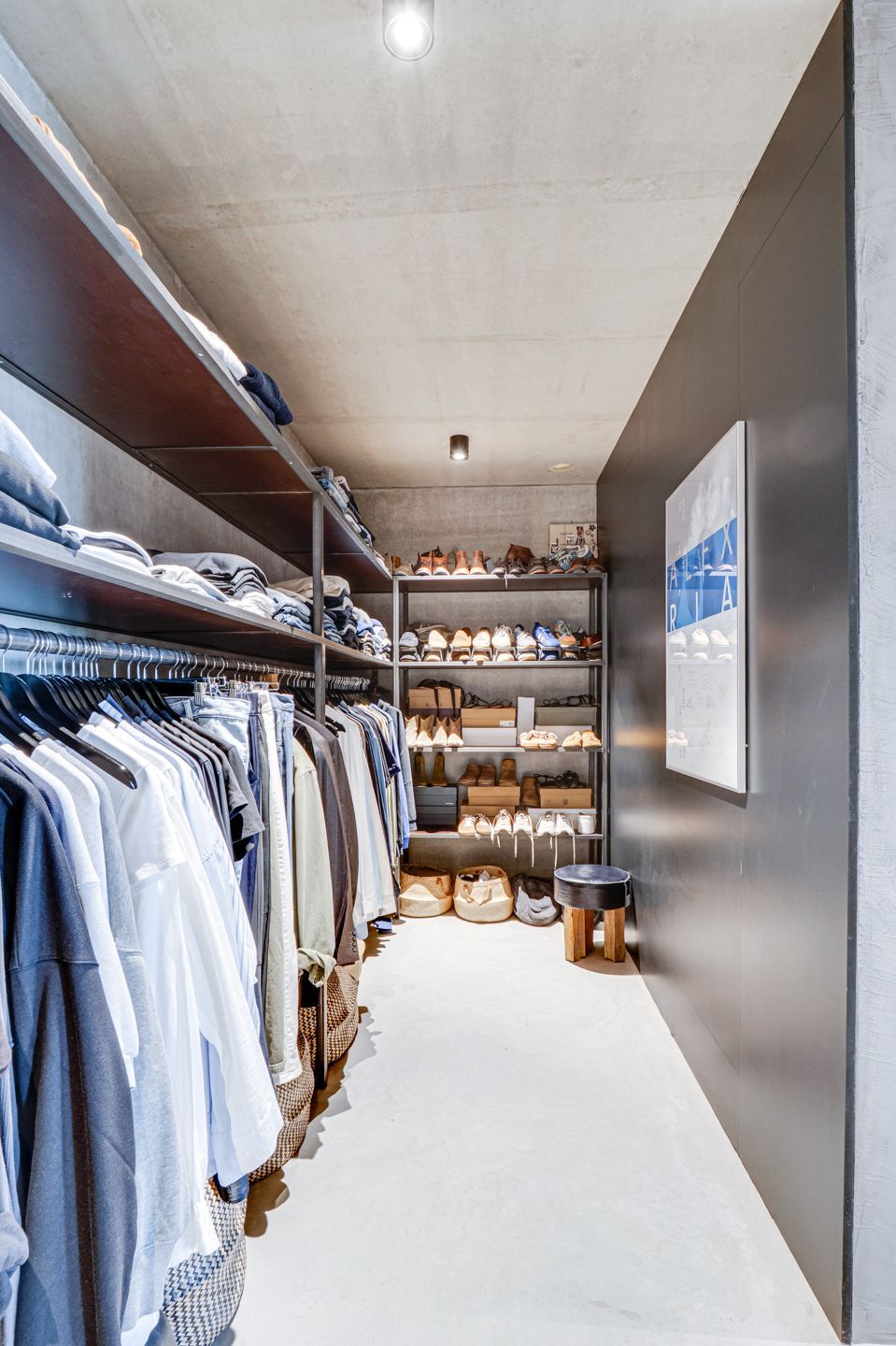 Moderne inloopkast met witte planken, hangende overhemden en opbergbakken in een smalle beige gang.