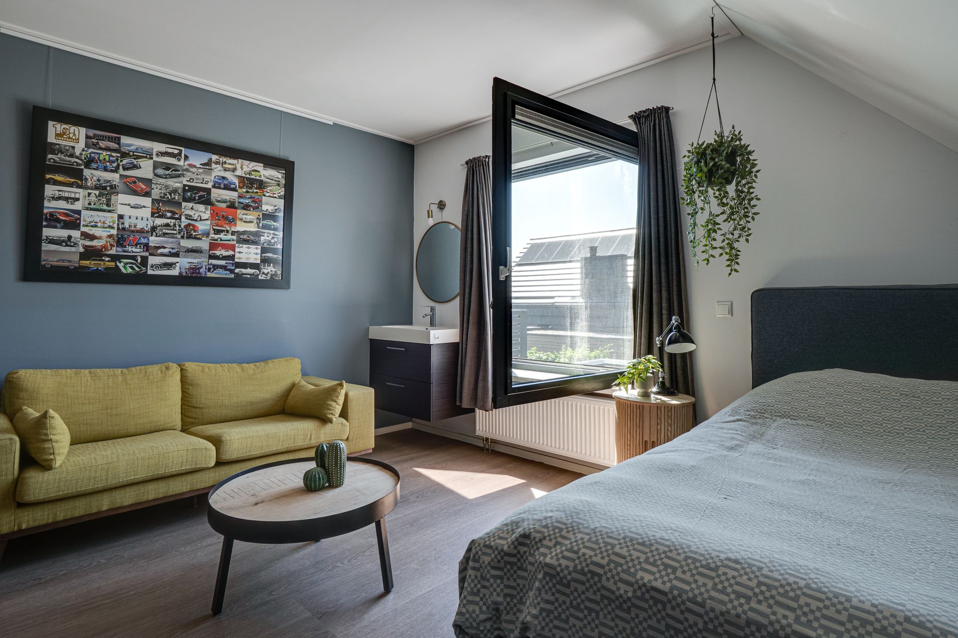 Moderne slaapkamer met openslaande balkondeuren, groene bank, ronde salontafel en hangplant.
