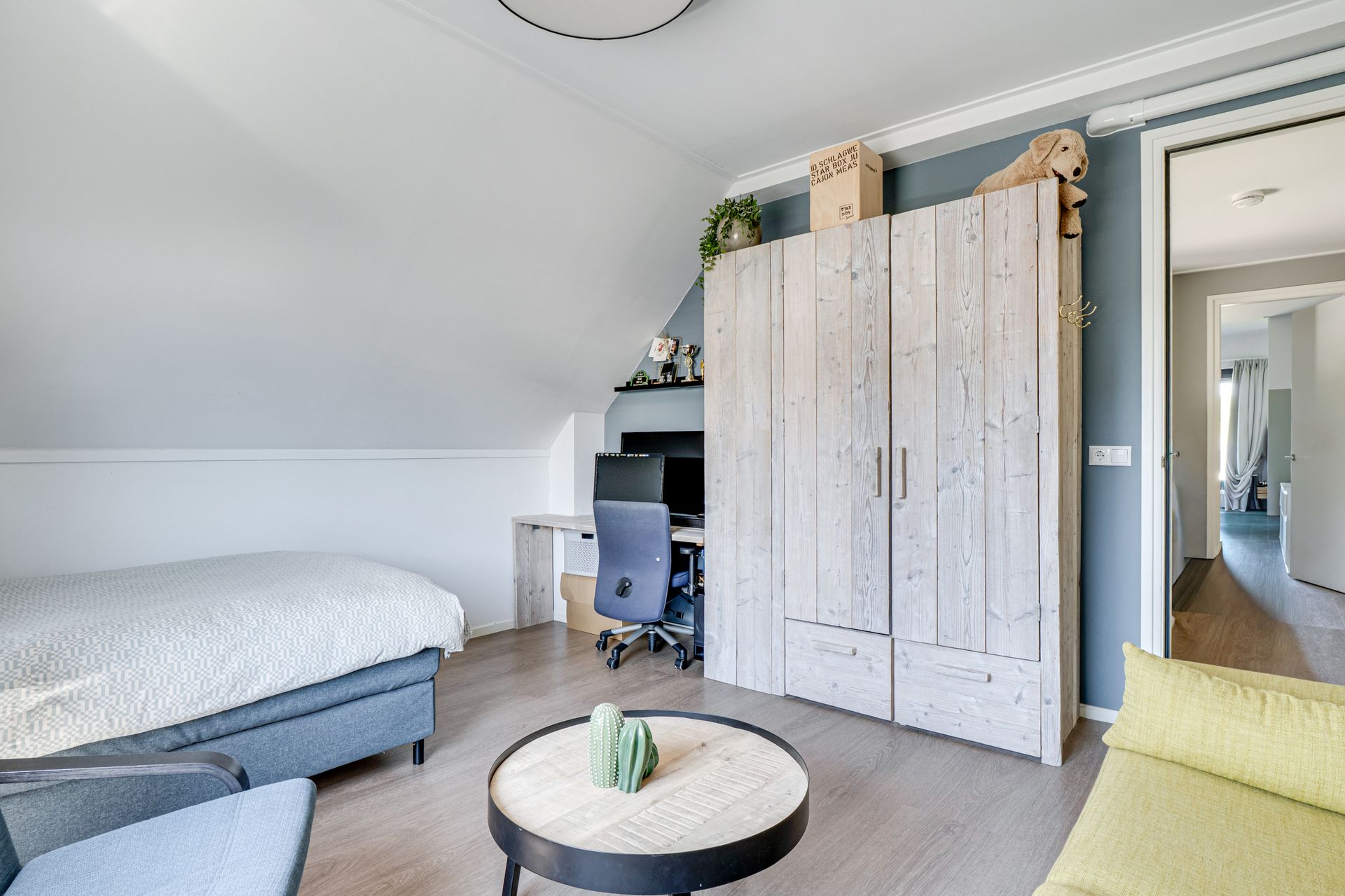 Kleine slaapkamer met een bed, bureau, kledingkast en ronde salontafel in neutrale tinten.