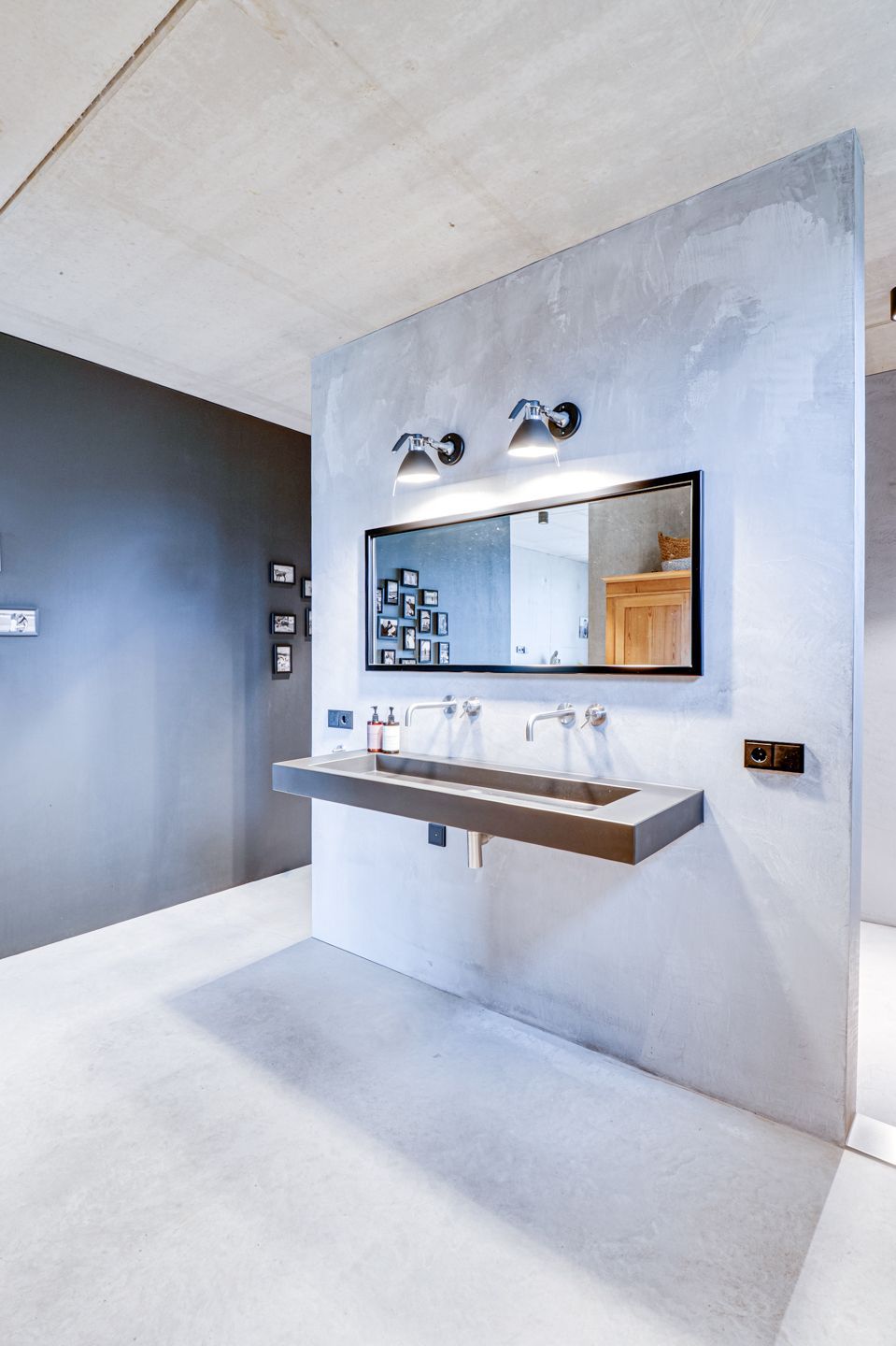 Moderne badkamer met grijze betonnen muren, wandgemonteerde wastafel, spiegel en zwarte accenten.