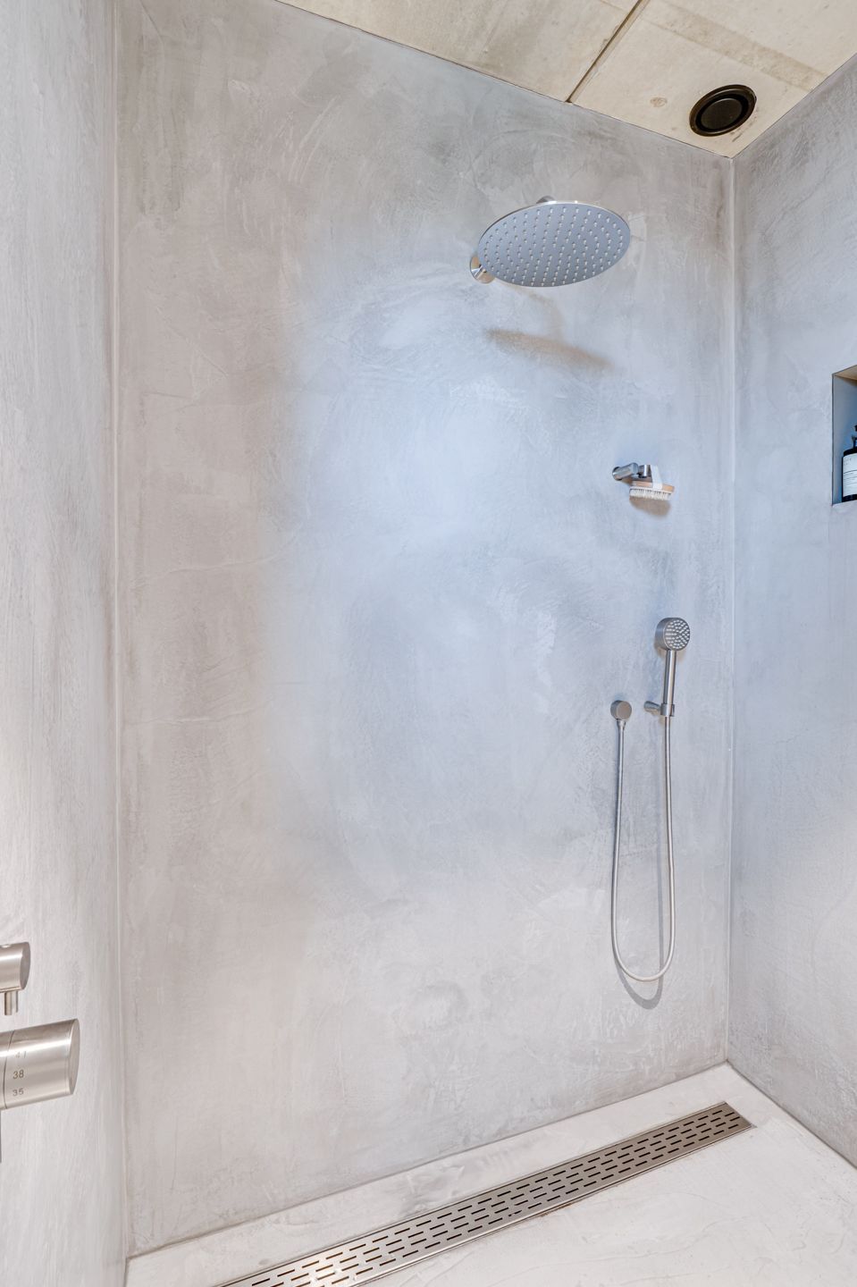 Moderne douche met lichtgrijze tegels, plafondafvoer, douchekop en lineaire vloerafvoer.