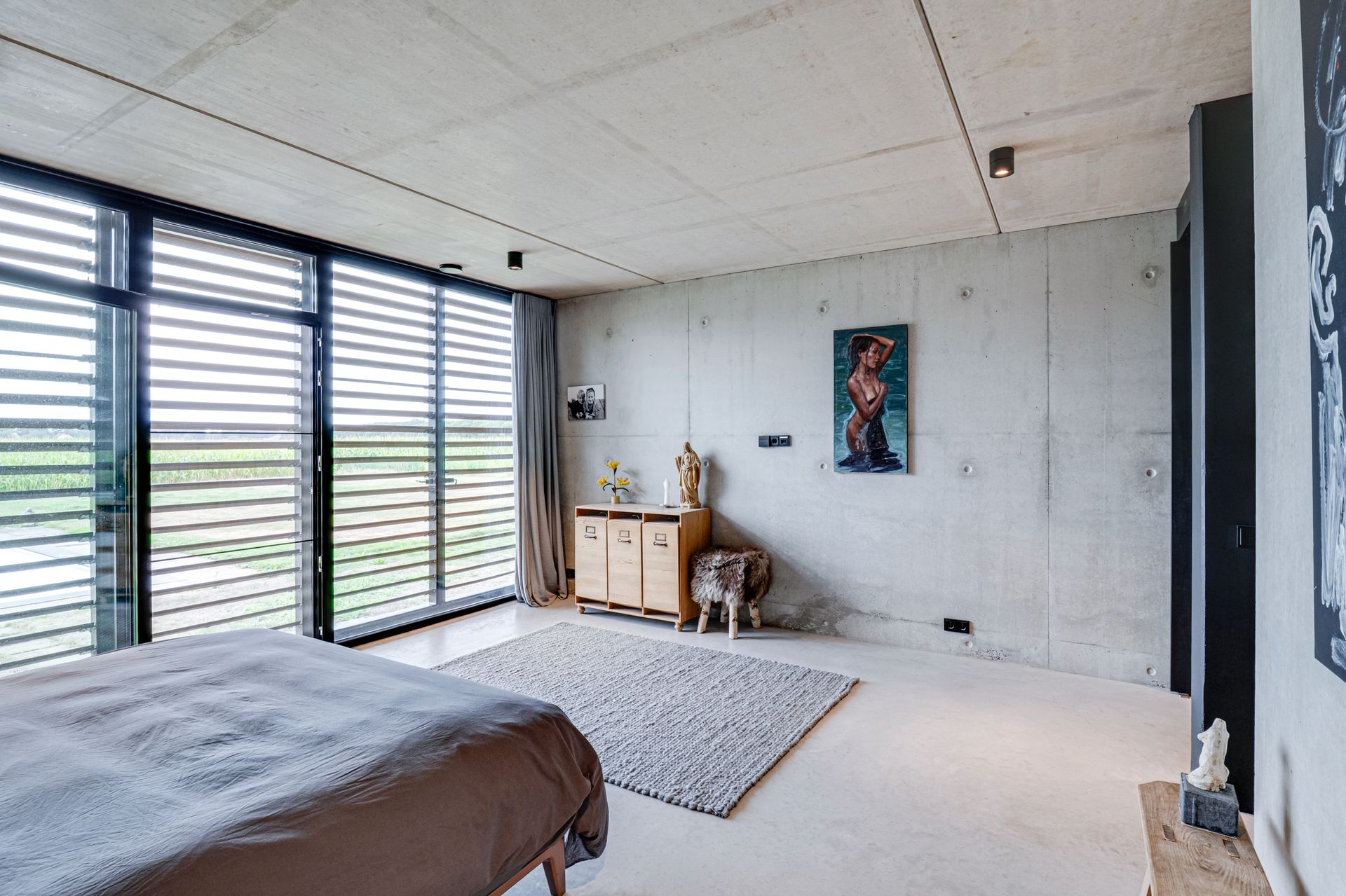 Moderne, minimalistische slaapkamer met grote ramen, bed, vloerkleed en een klein houten bureau tegen de muur.