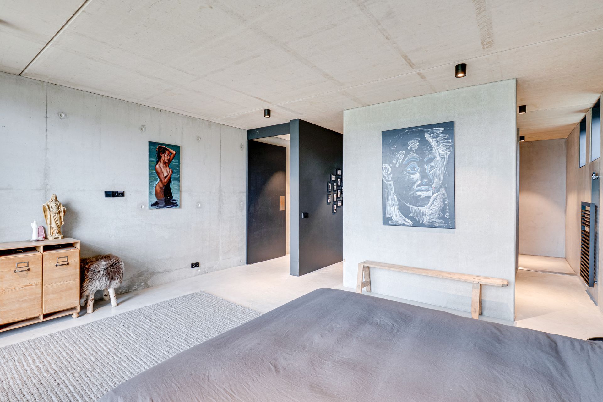 Moderne woonkamer met witte muren, een grijze bank, wanddecoratie en een klein hondje bij een houten kast.