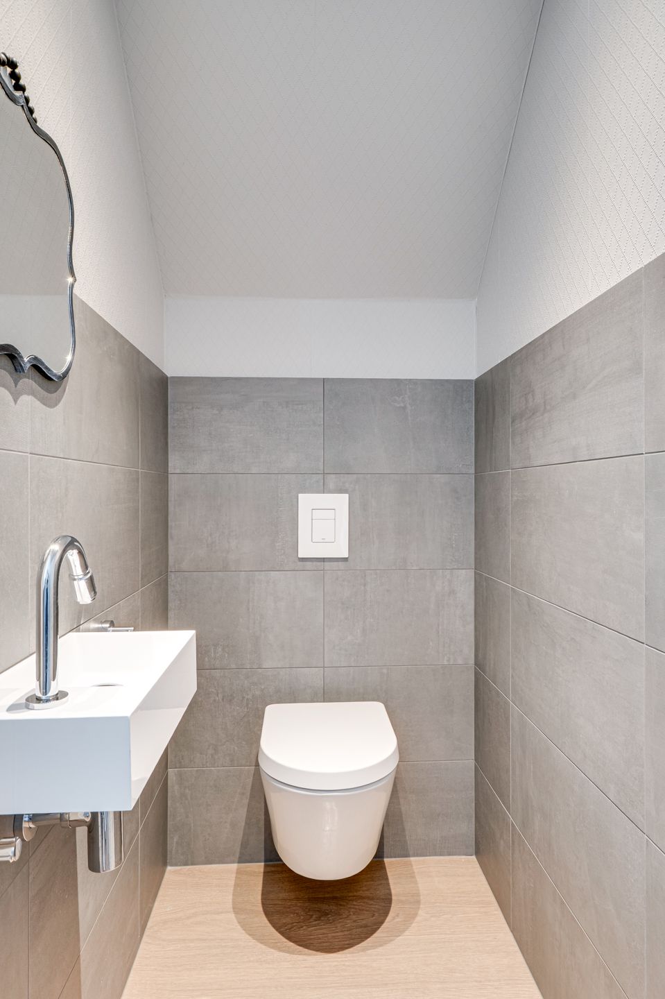 Kleine, moderne badkamer met een aan de muur gemonteerd toilet en wastafel, grijze tegelwanden en een wit plafond.