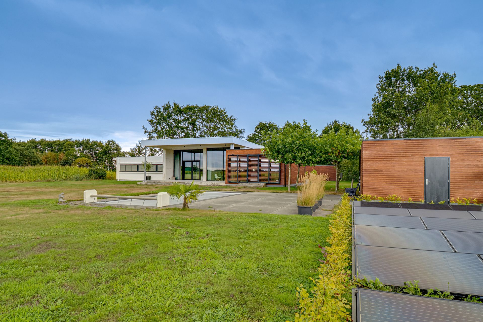 Modern huis met een grasveld, een bakstenen muur en een geplaveide oprit onder een blauwe hemel.