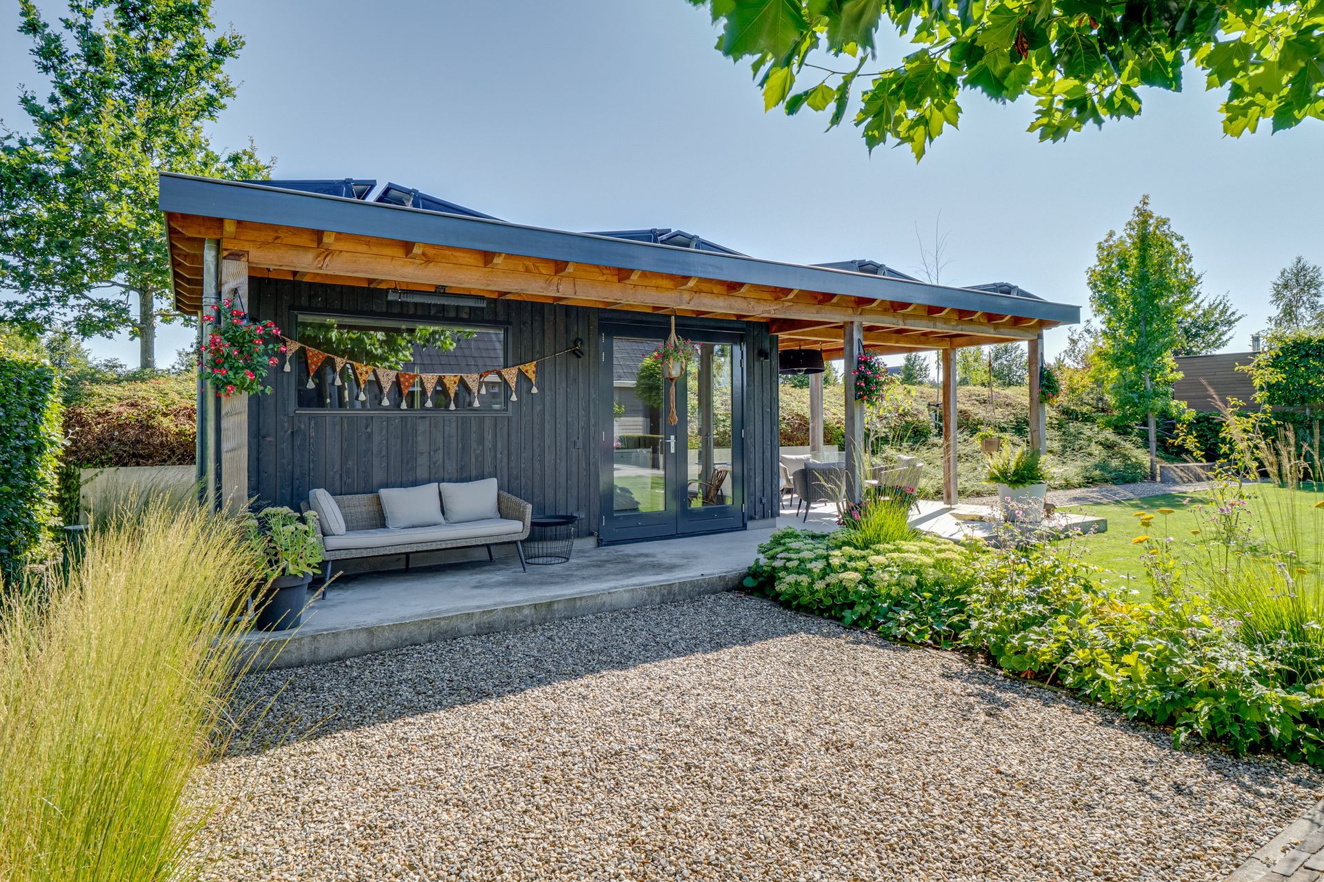 Moderne woning met overdekt terras, grindpad en aangelegde tuin, badend in de zon.