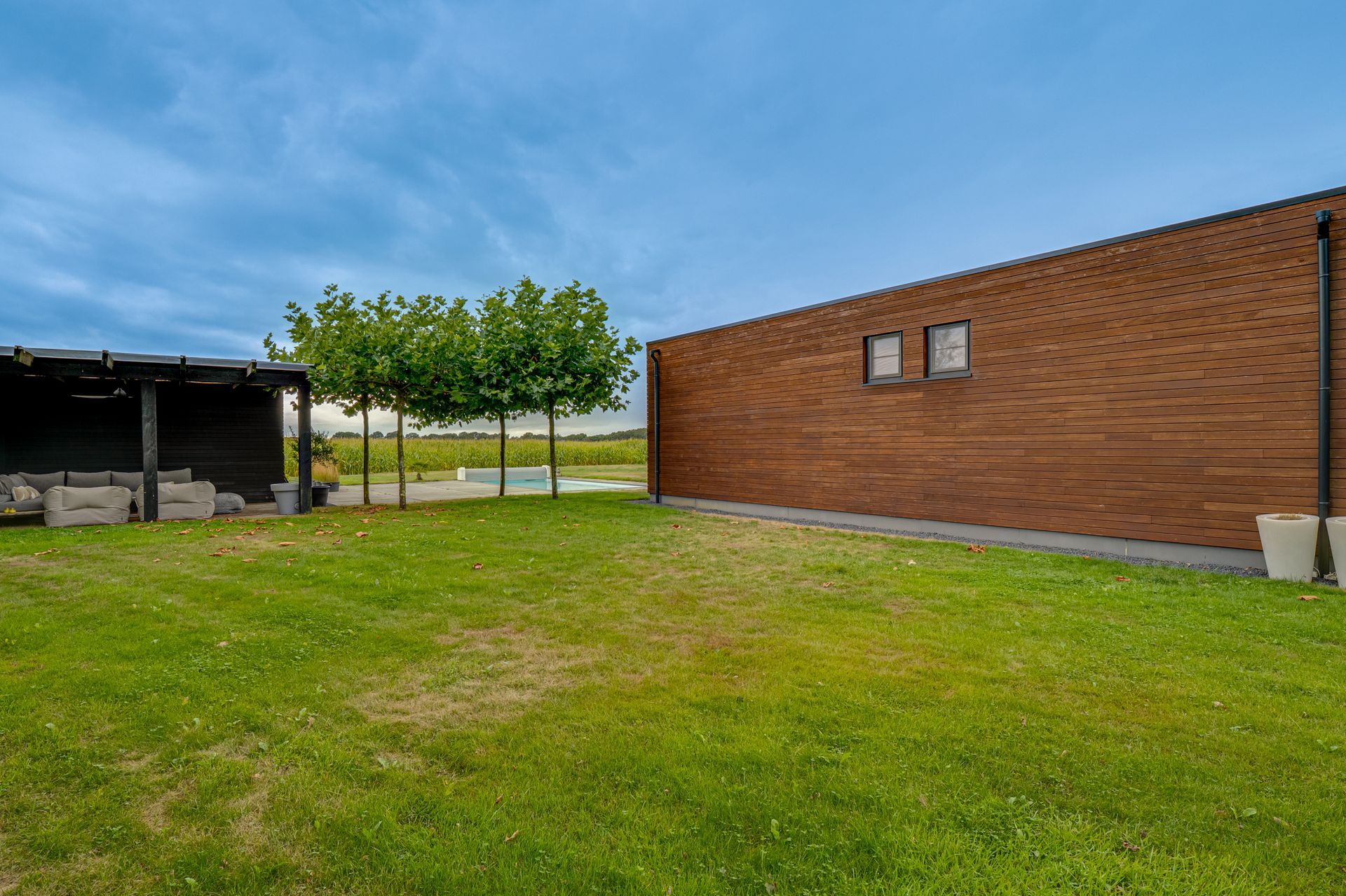 Een grasveld naast een bakstenen gebouw en een overdekte schuilplaats onder een gedeeltelijk bewolkte hemel.