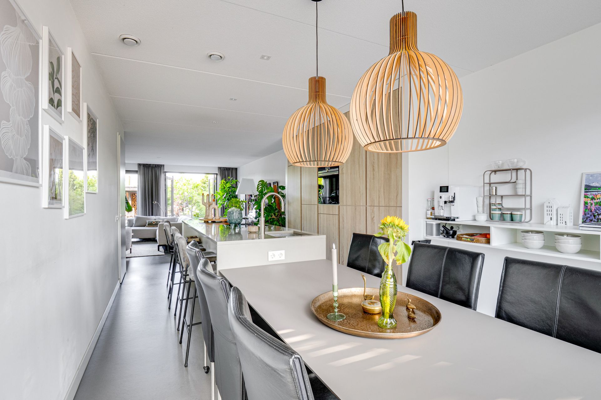 Moderne open eetruimte met witte muren, grijze zitmeubels en geweven hanglampen.