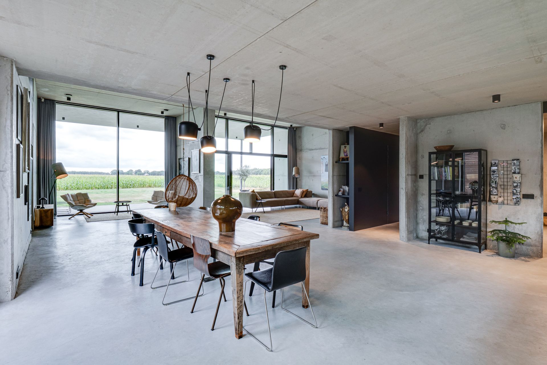 Moderne open eetkamer met een lange houten tafel, zwarte stoelen en grote ramen met uitzicht op een veld.