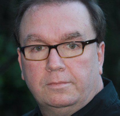 Close-up portrait of a person wearing black glasses, neutral expression, dark blurred background