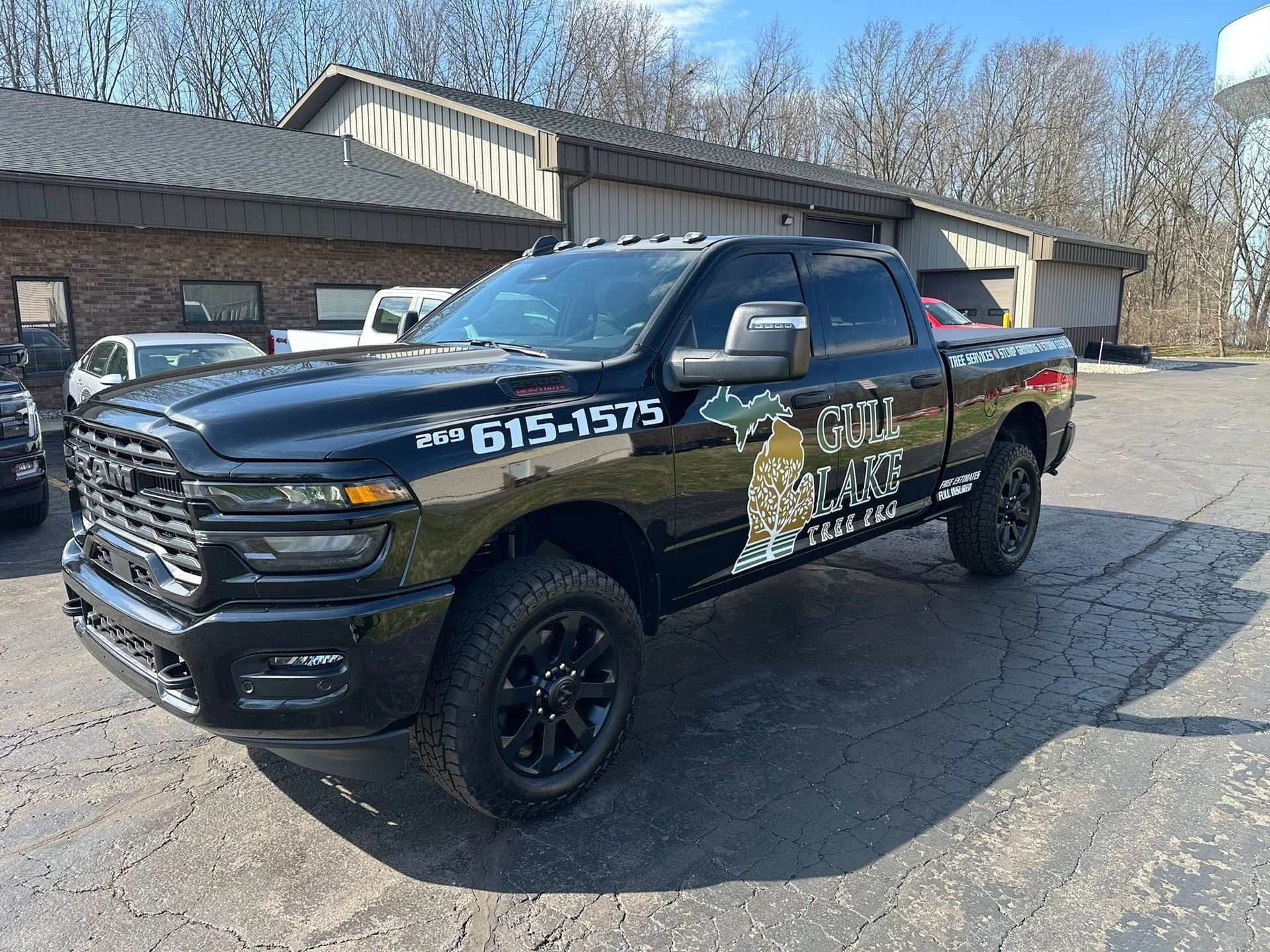 Black pickup truck with company graphics parked outside a building on a gravel lot.