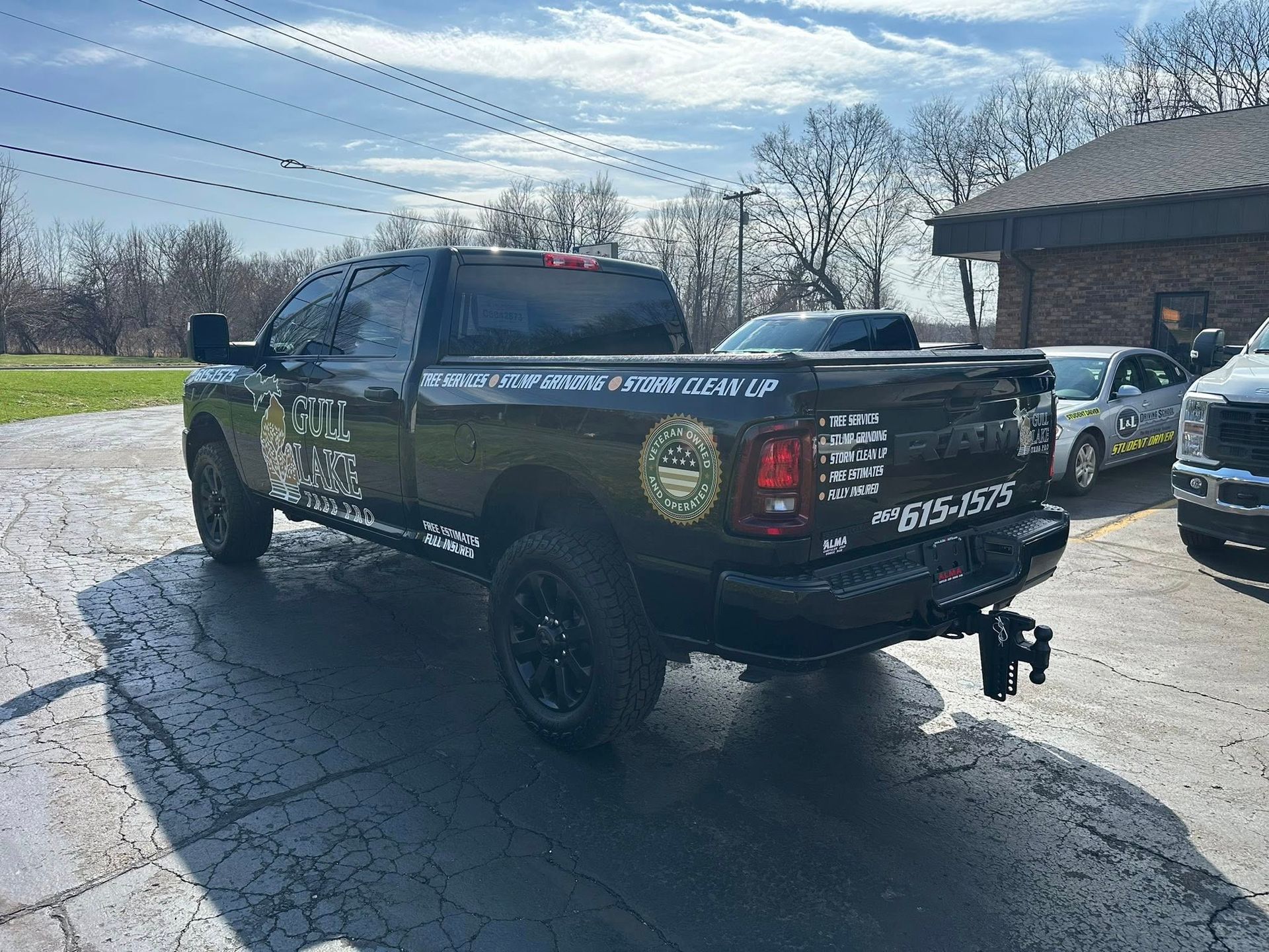 Black pickup truck with decals parked on wet pavement beside another vehicle under a cloudy sky