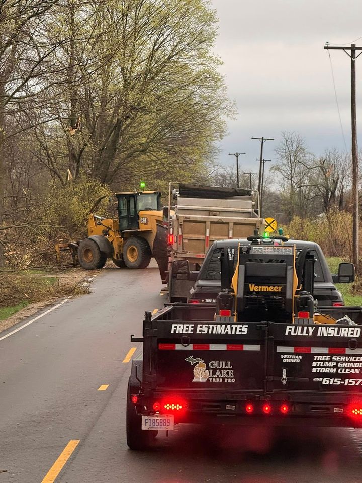 Roadside work crew with loader and trucks blocking a lane on a tree-lined road