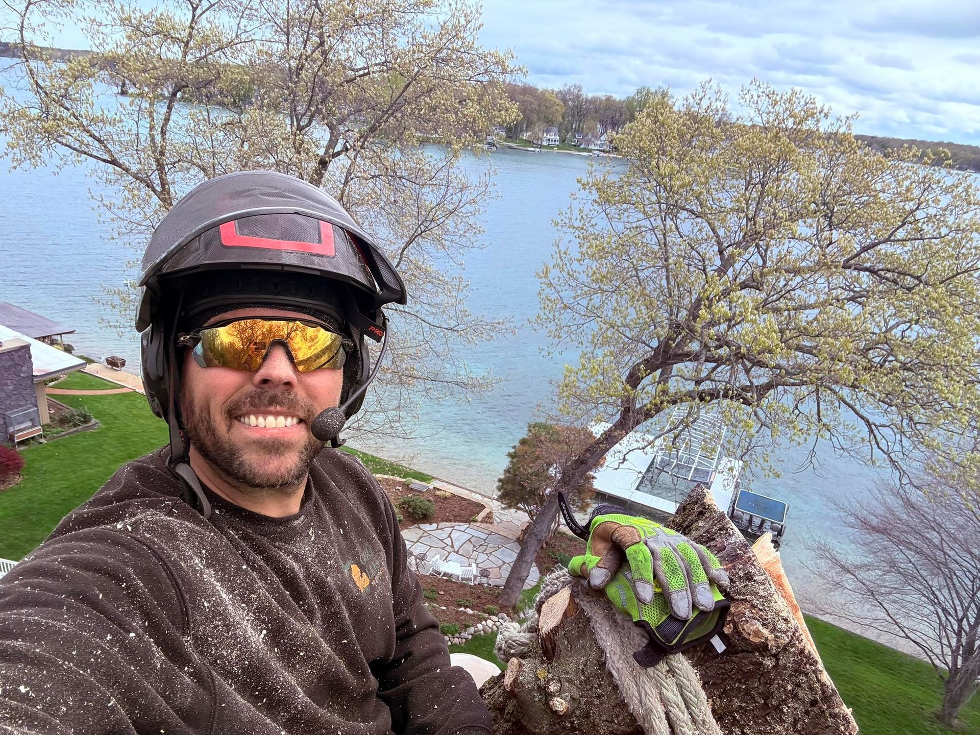 Helmeted cyclist taking a selfie by a lake, holding a bright green glove, with water and trees behind.