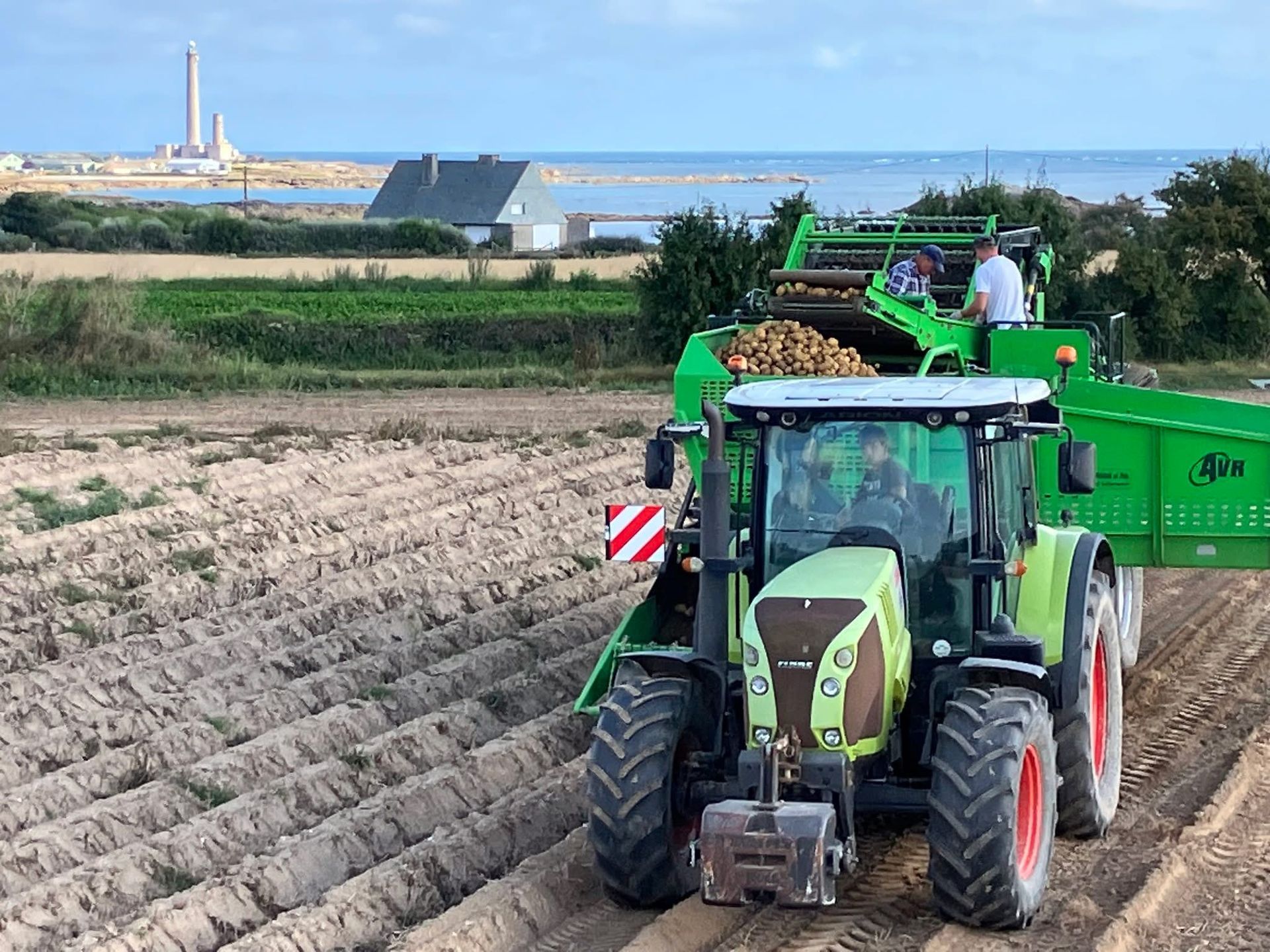 Un tracteur vert tire une arracheuse de pommes de terre dans un champ. La machine extrait les pommes de terre.