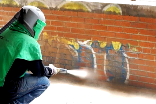 Contact Us A man is sandblasting graffiti on a brick wall.
