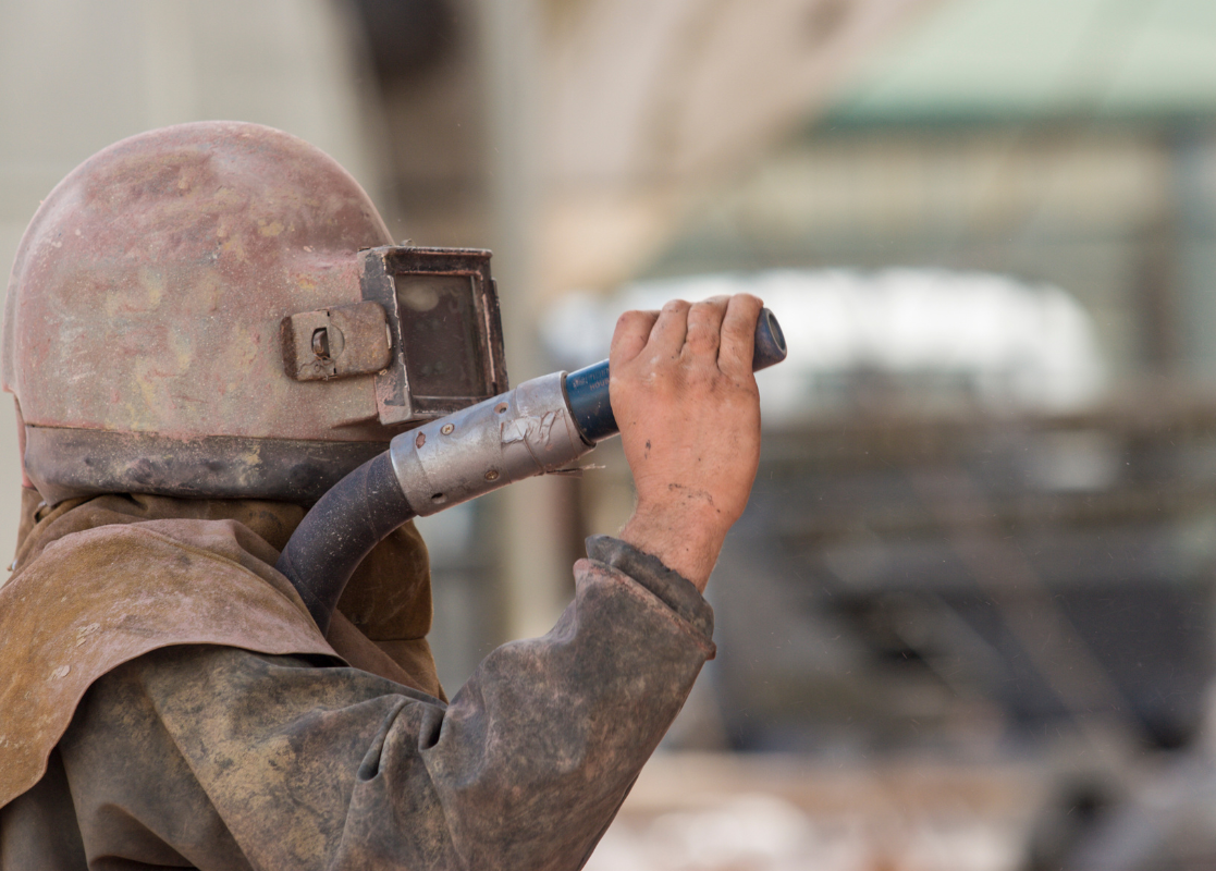 A person wearing a helmet and goggles is sandblasting a car.