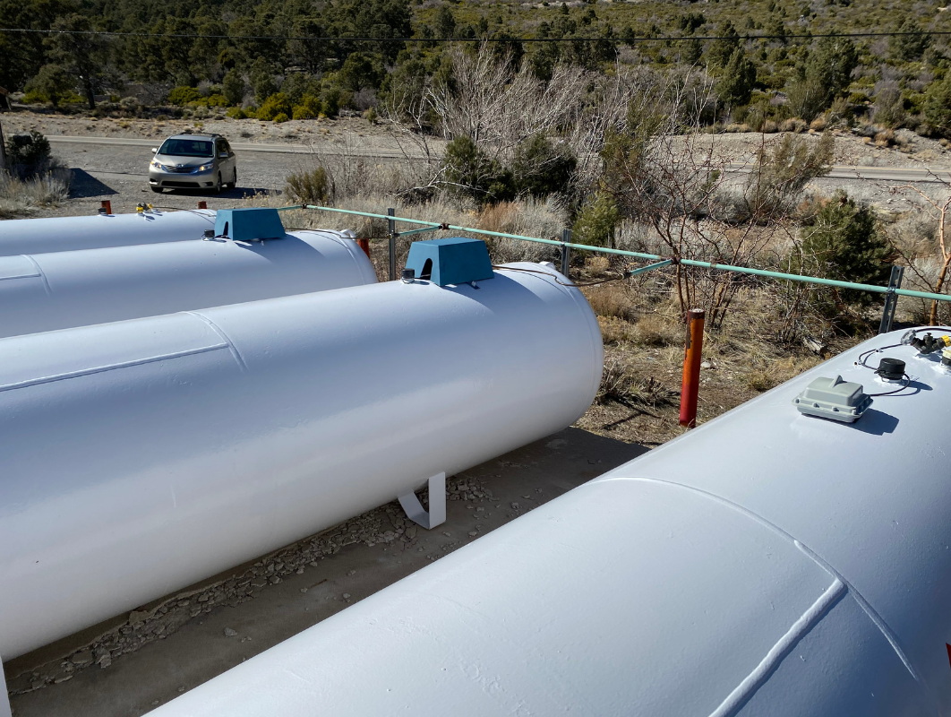 A row of white propane tanks are lined up in a field.