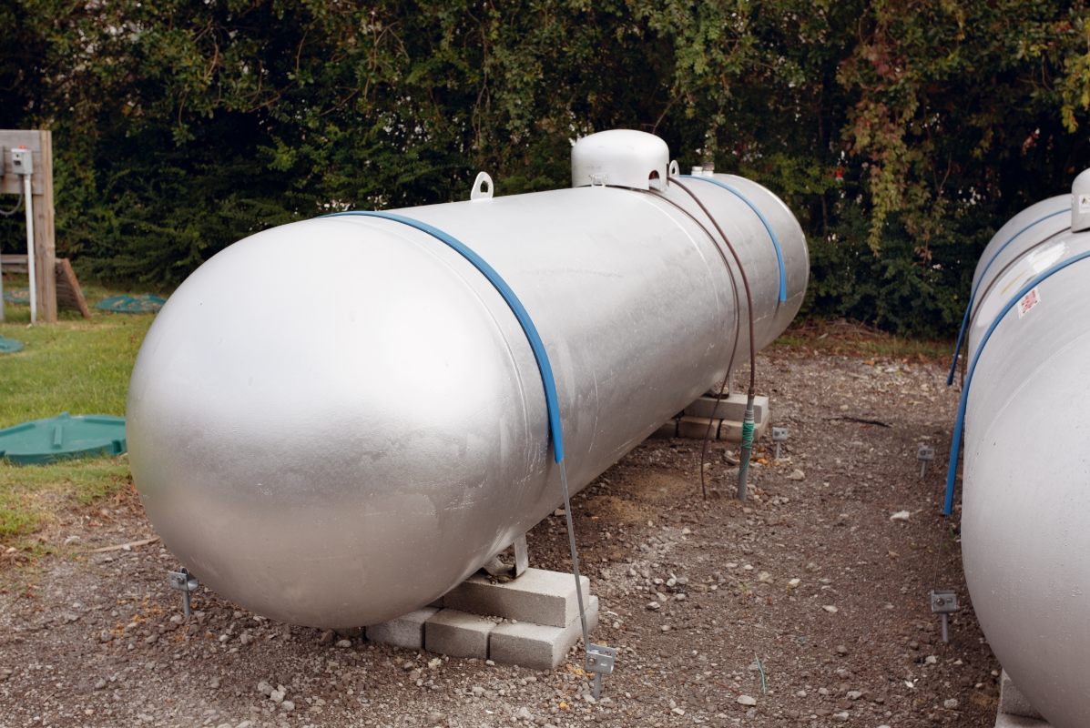 A large propane tank is sitting on top of a gravel lot.