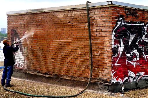 Contact Us A man is spraying graffiti on a brick wall with a hose.