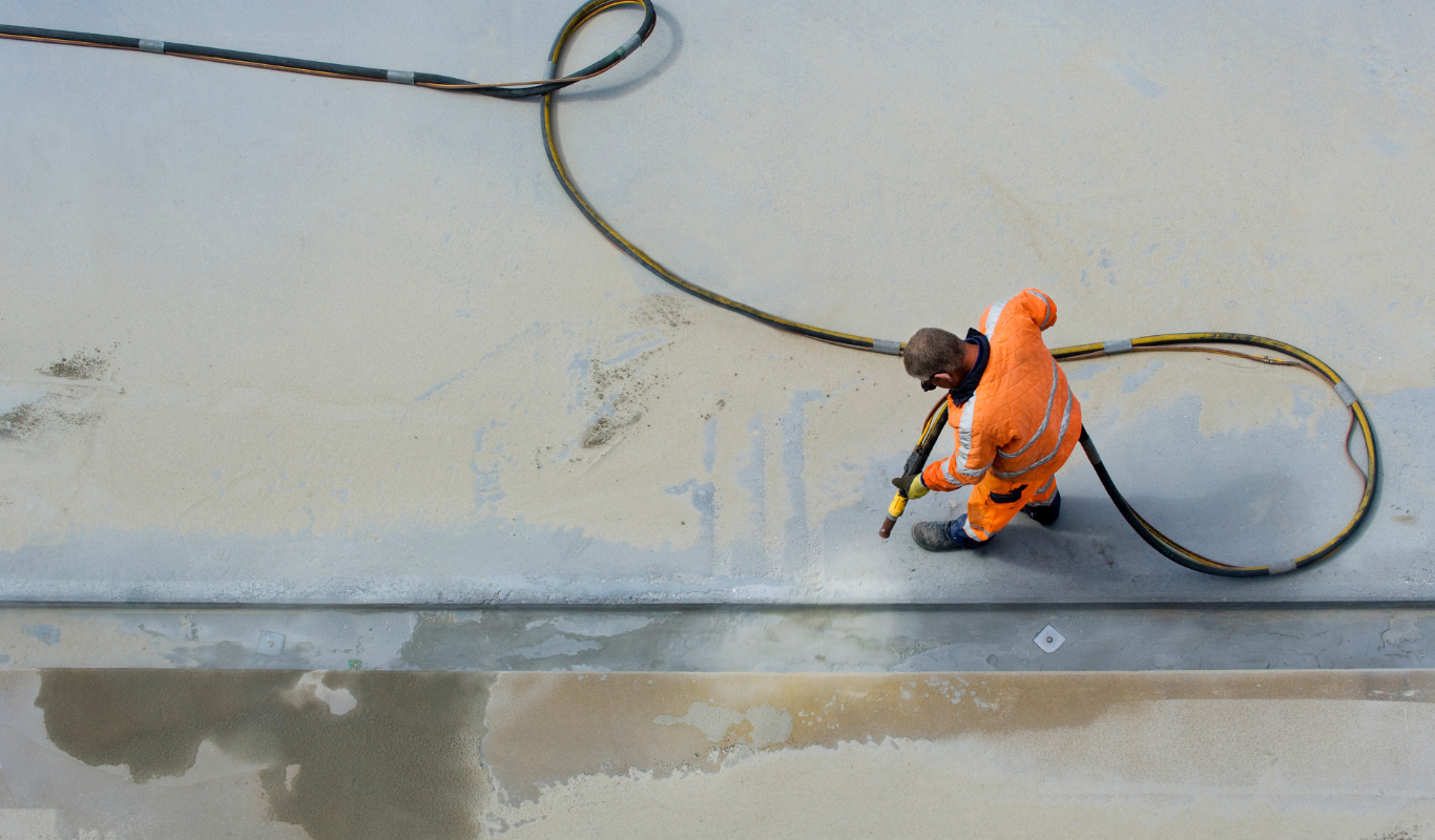 A man in an orange suit is cleaning a concrete surface with a hose.