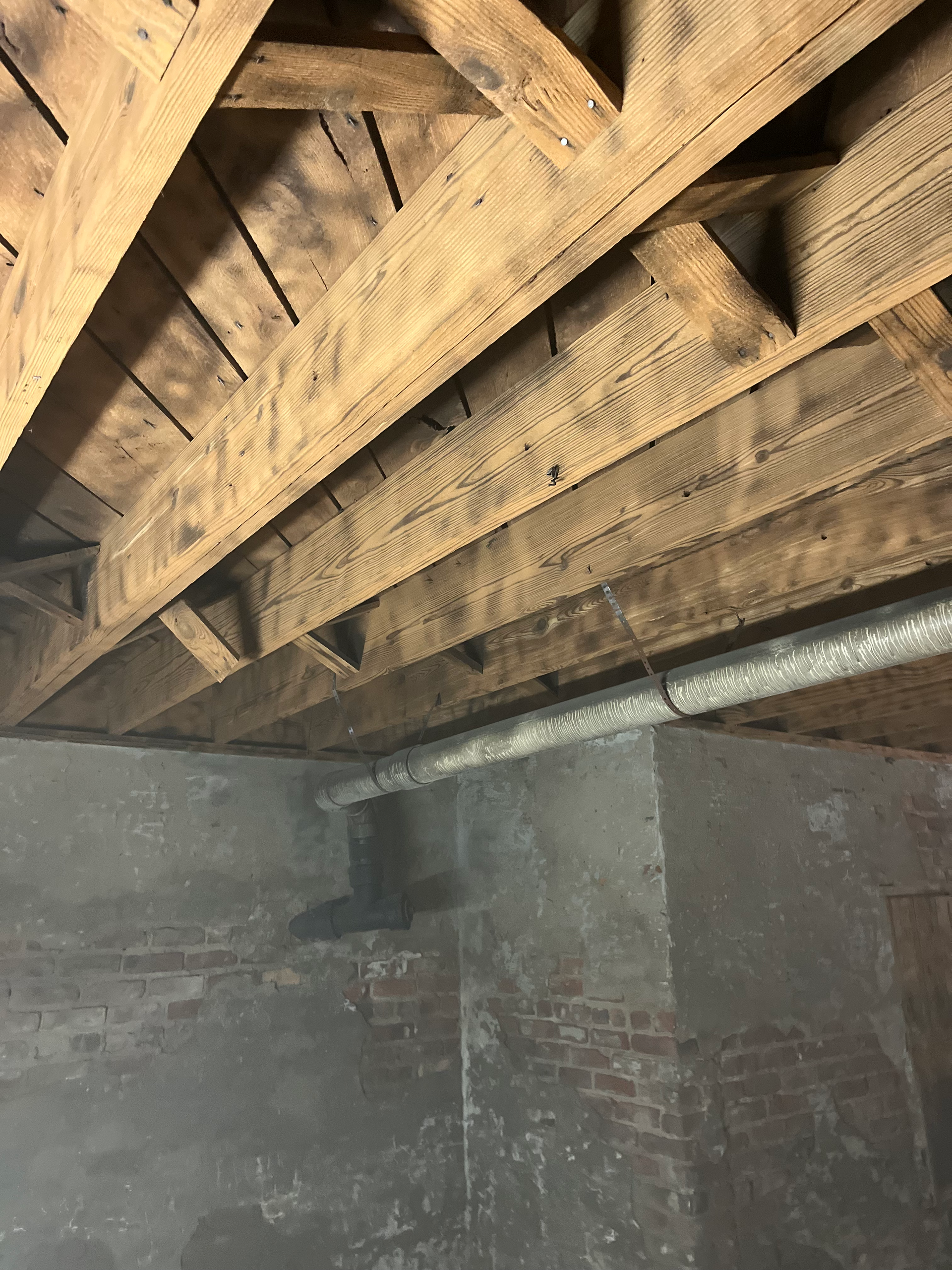 The ceiling of a basement with wooden beams and a brick wall.