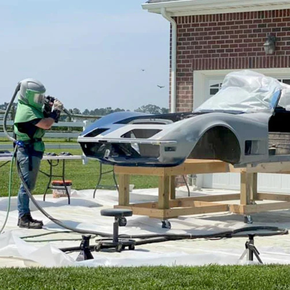 A man wearing a helmet is sandblasting a car